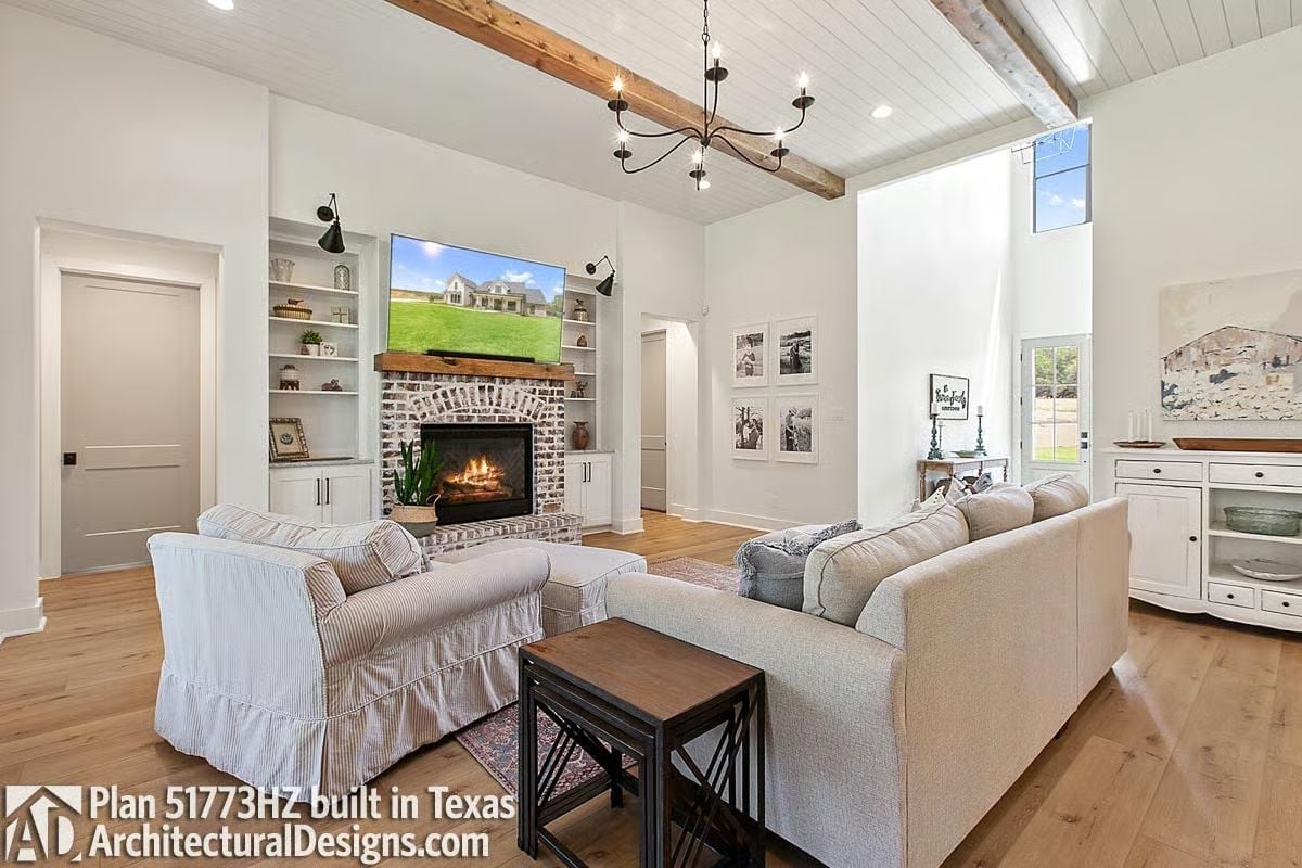 Brick Fireplace, Skirted Chairs, and Ceiling Beams Walk Into a Living Room
