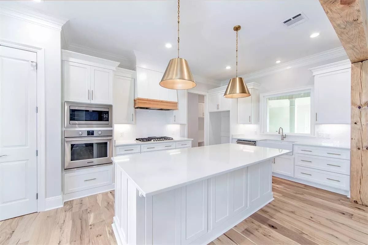 Brass Pendants and a Wood Range Hood Pull Warmth Into an All-White Kitchen