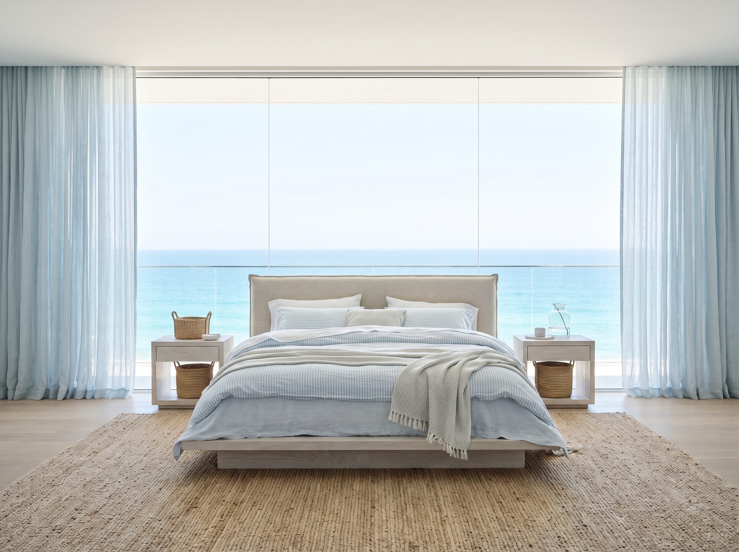 Coastal bedroom with a low upholstered bed set beneath a wide window, its headboard stopping below the sill so the water