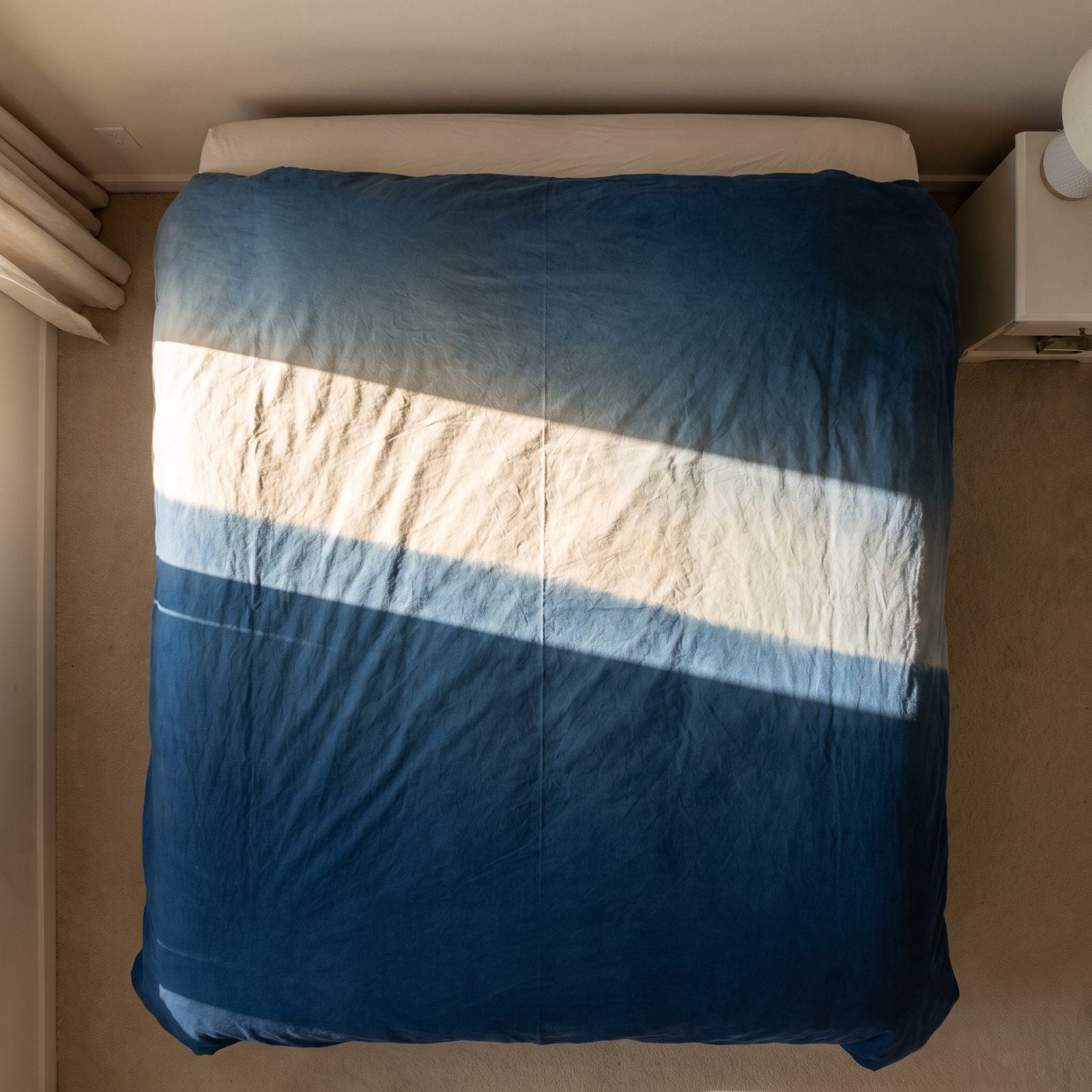 Bedroom with a bed under a west-facing window where the top of the duvet has faded lighter than the bottom.