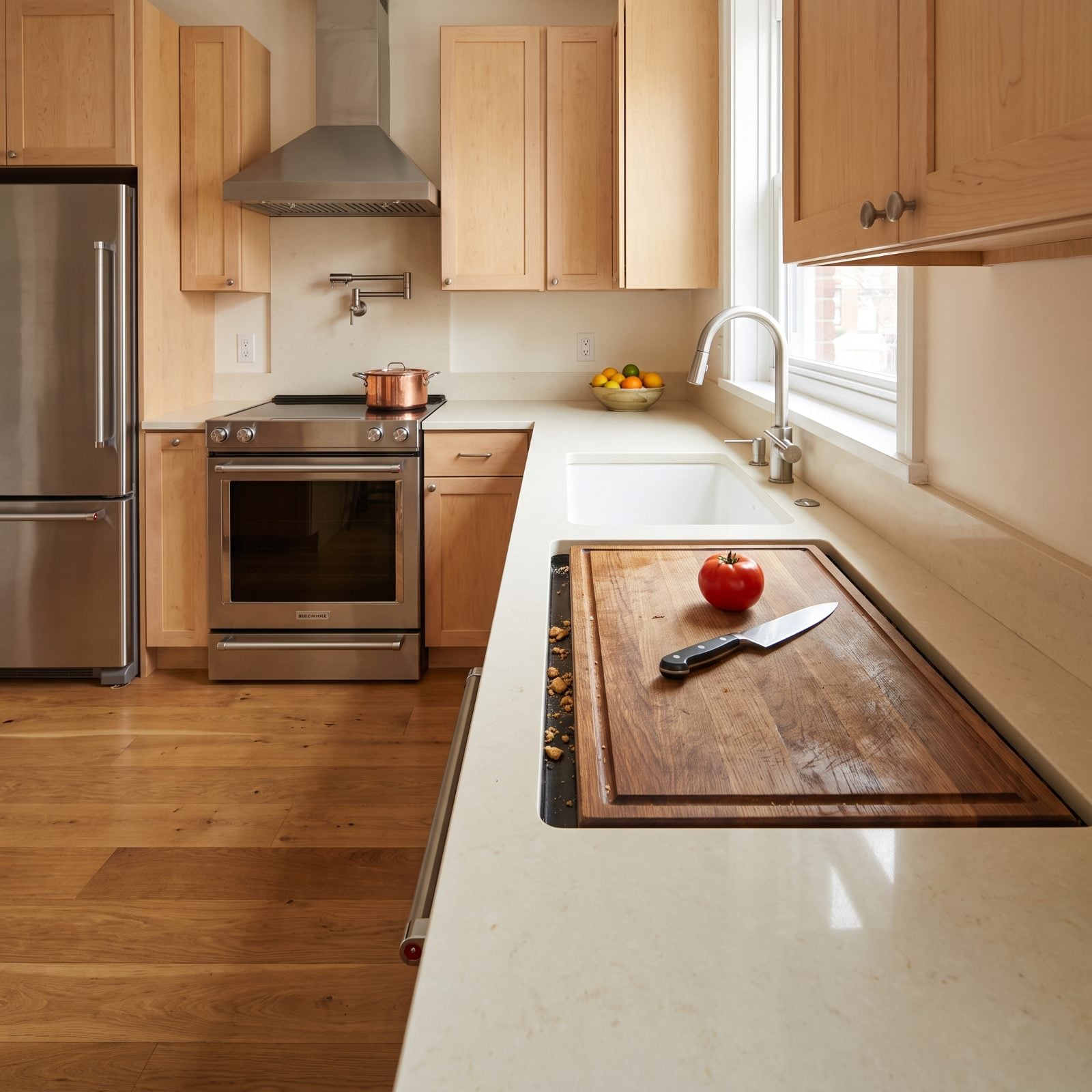 Oak kitchen with a built-in wooden cutting board set flush into the counter, showing a seam where crumbs collect.