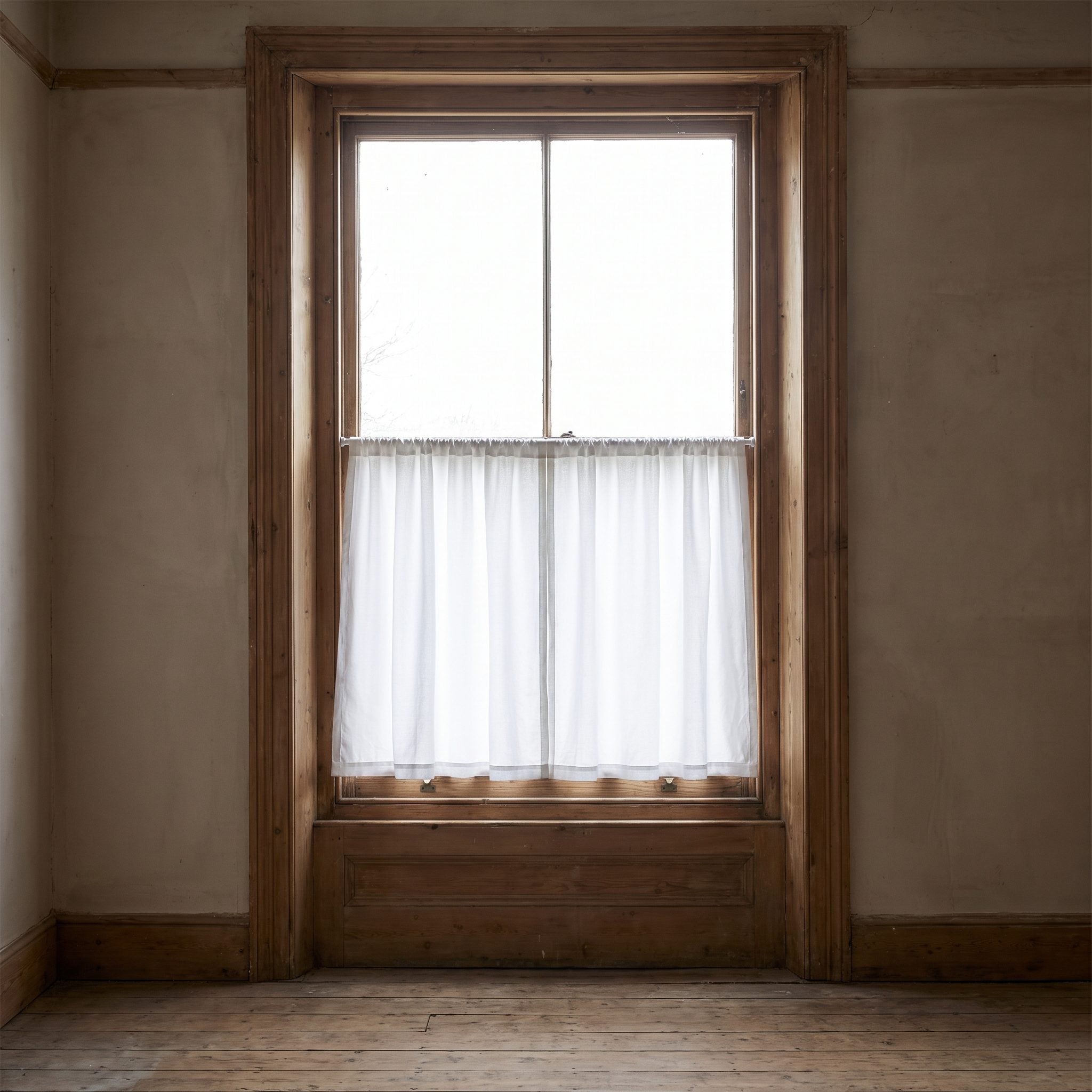 Kitchen window over the sink with a linen café curtain covering the lower half and the upper half of the glass left