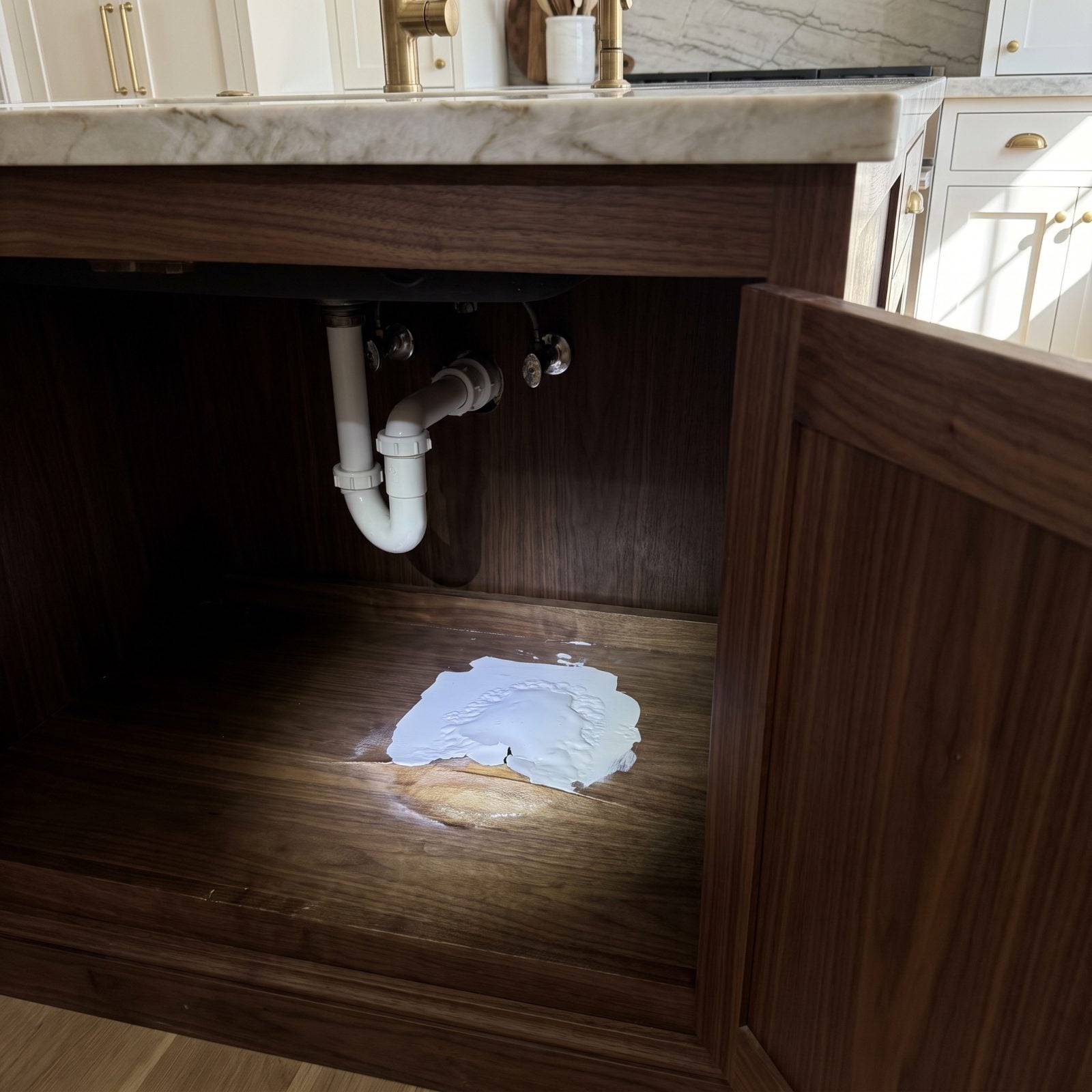 White kitchen sink cabinet with a freshly painted exterior and a dark swollen water stain on the interior floor near the