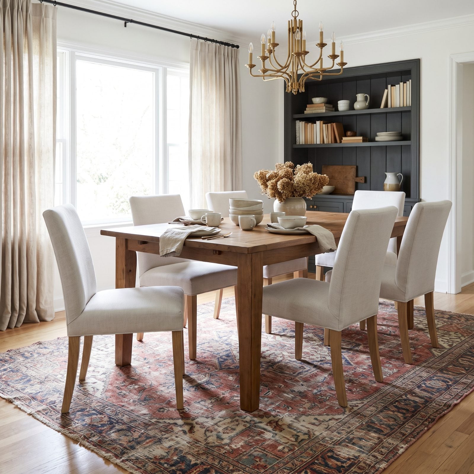 Bright dining room with new cream boucle chairs and a heavily worn antique Persian rug faded and frayed under the table.