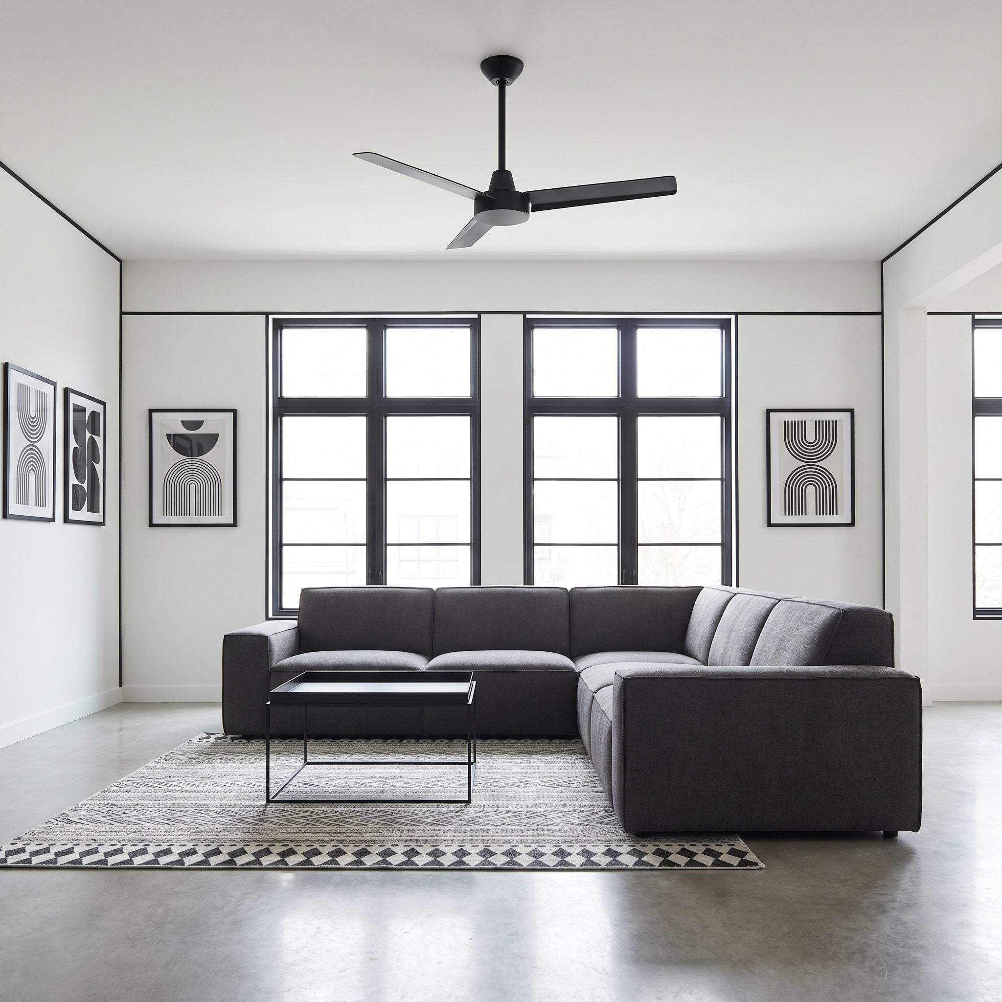 Living room with a black-bladed ceiling fan whose finish matches the black window frame, curtain rod, and door handles in