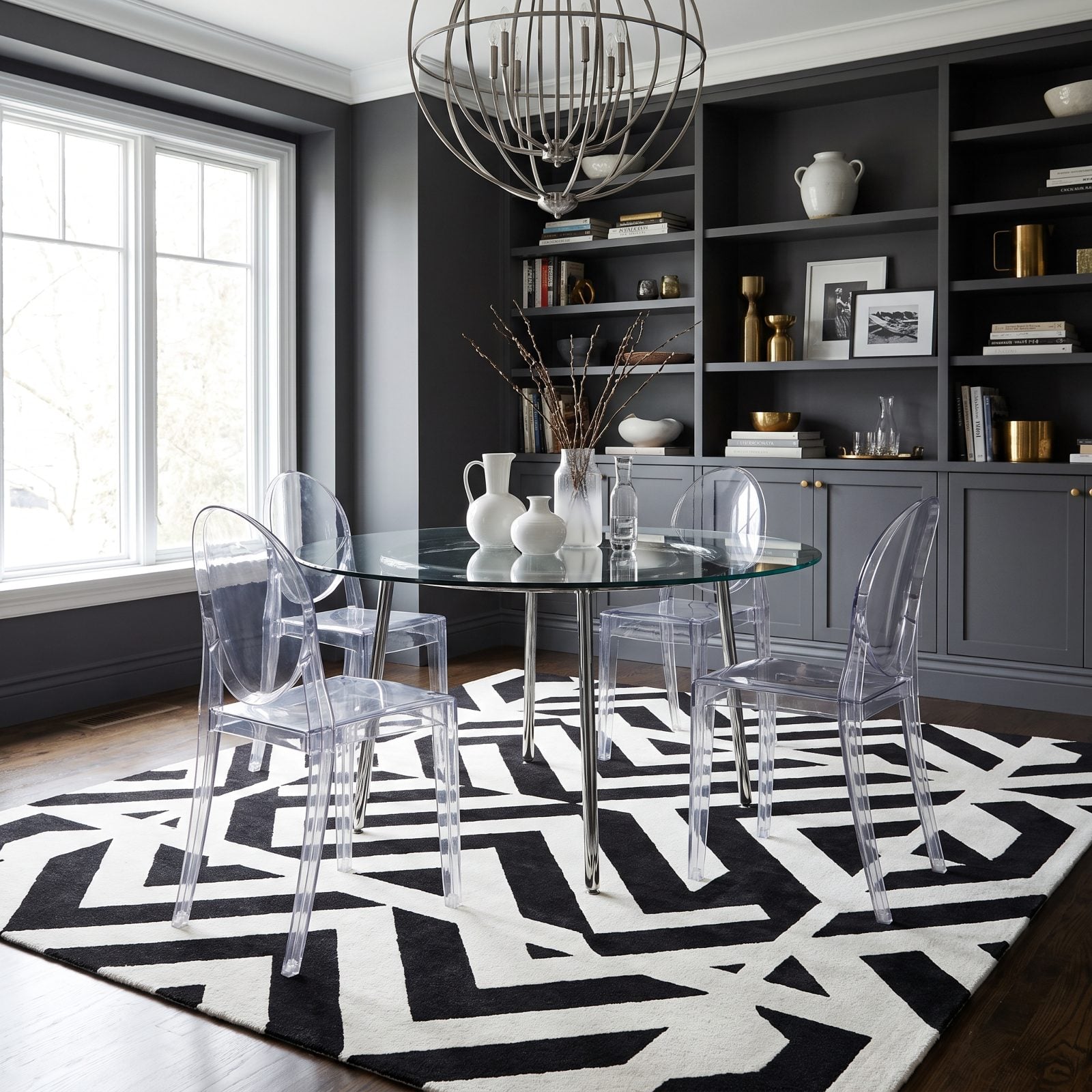 Modern dining room with a delicate glass table on brass legs sitting over a bold high-contrast black-and-white geometric rug