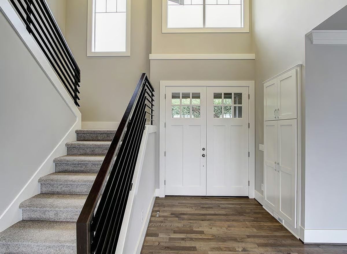 Soaring Two-Story Foyer With Craftsman Double Doors and Dark Wood Stair Rail