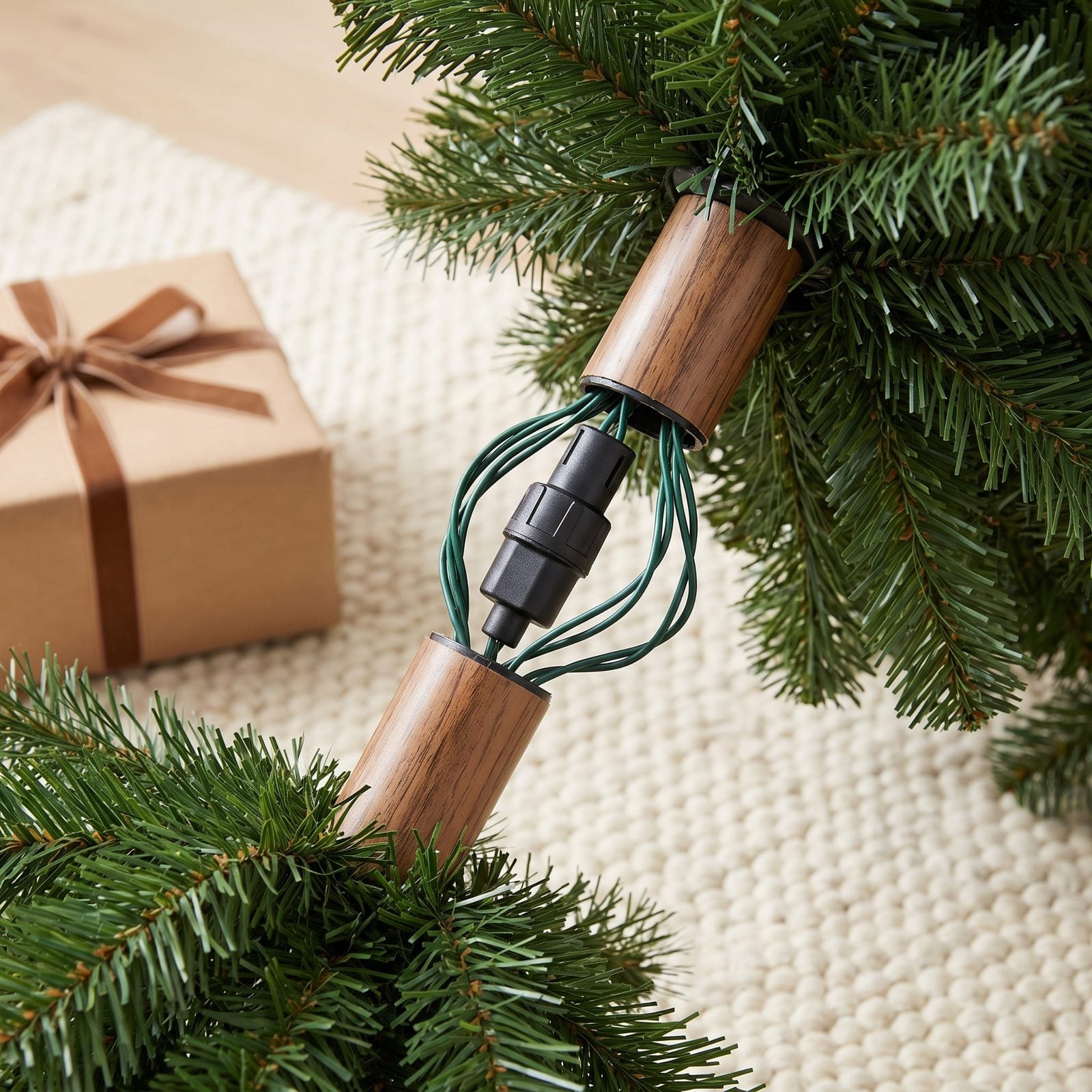 Pre-lit artificial tree trunk with black electrical connector plugs and looping green wire exposed between the branches.