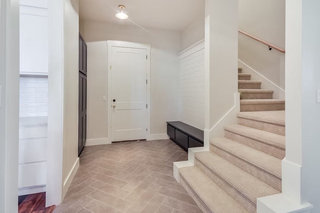 Herringbone Tile and a Carpeted Stair Make This Mudroom Entry Work Hard