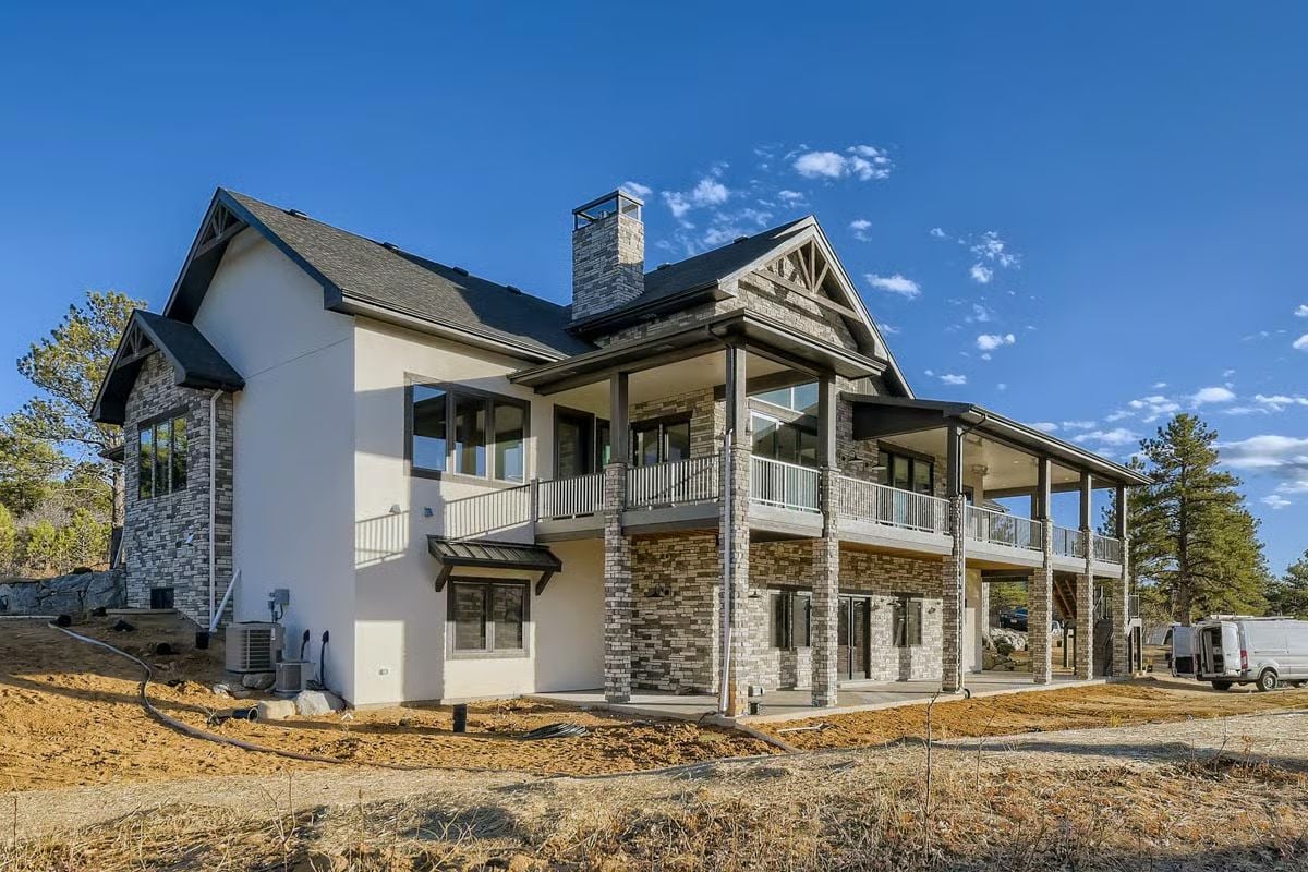 Stone Columns, Wrapped Porch, and a Roofline That Means Business