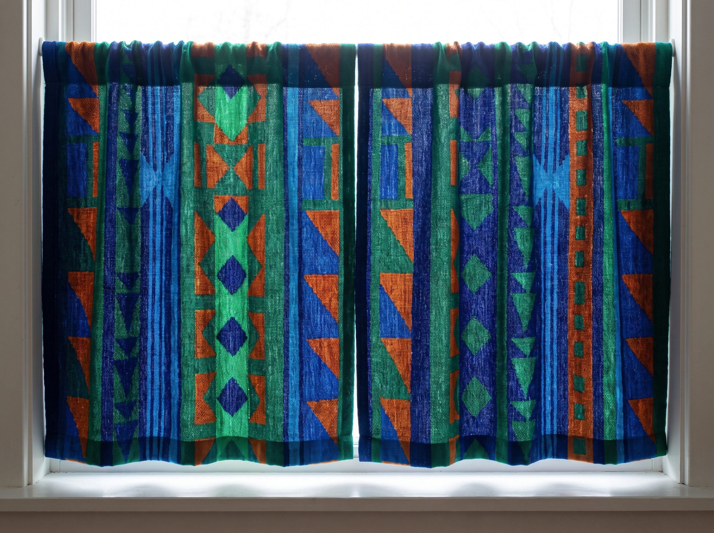 Kitchen with a blue-and-white block-print café curtain hung above the sink and hemmed at the windowsill on a brass rod.