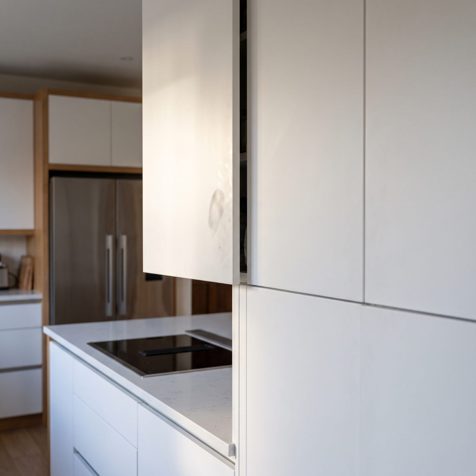 Handleless white kitchen with a push-to-open cabinet ajar and faint fingerprints on the door fronts.