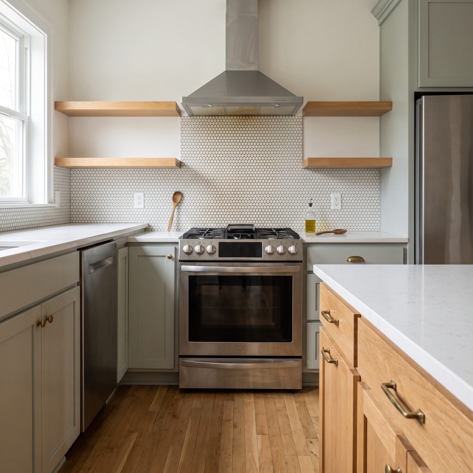 Grey-green kitchen with a one-inch penny-round mosaic backsplash behind the range showing faint residue in the grout lines.