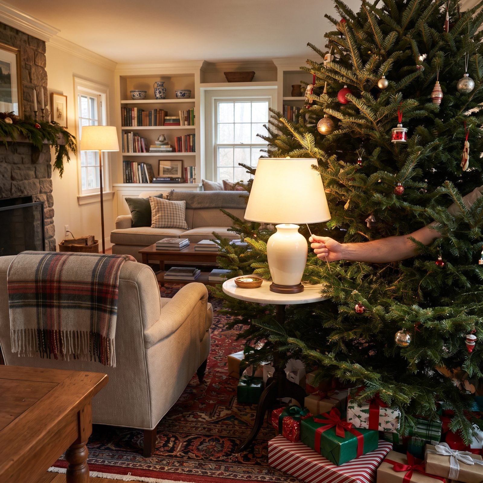 Small living room with a decorated Christmas tree standing in front of a walnut side table and its lamp.
