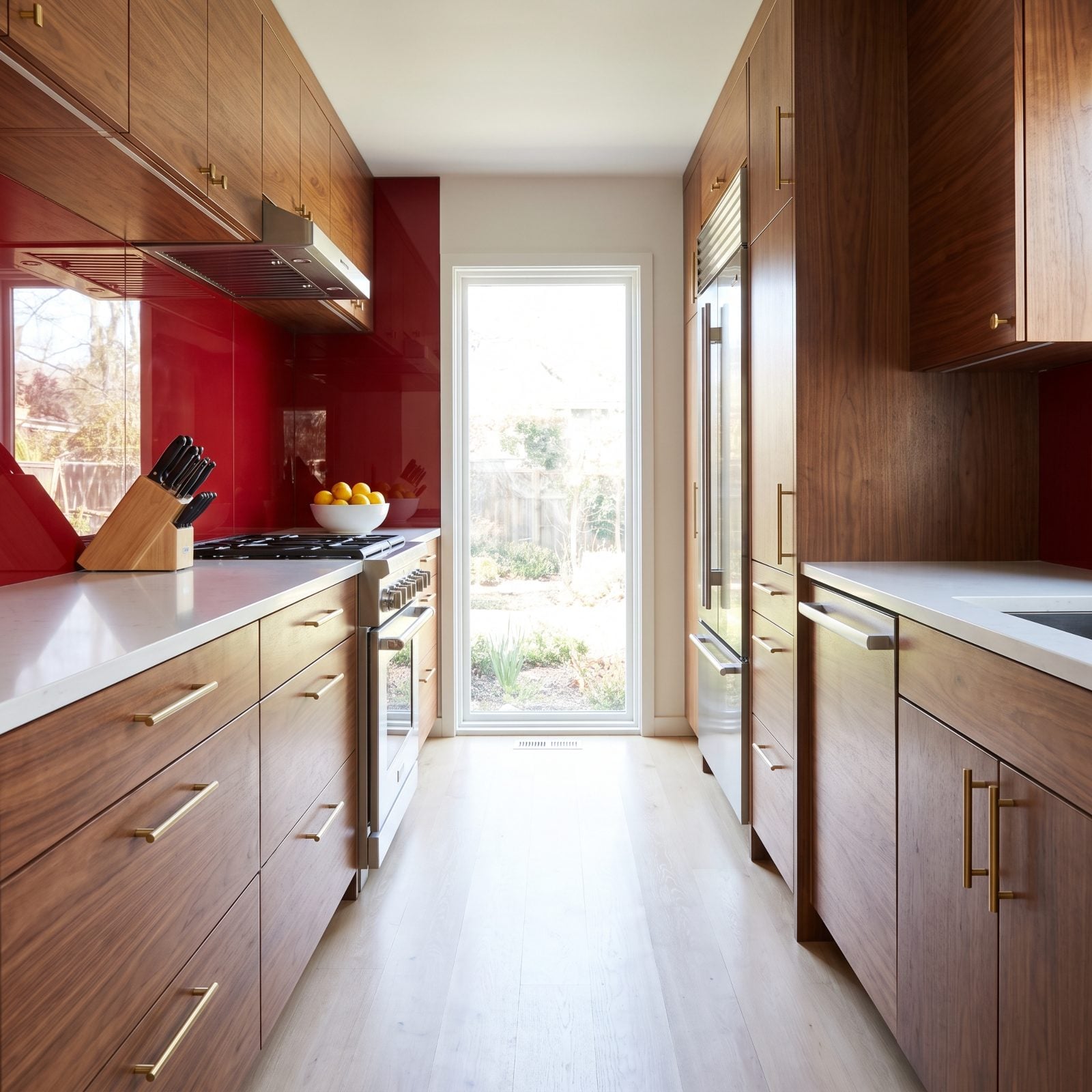 Walnut Galley Kitchen With a Glossy Cherry-Red Backsplash