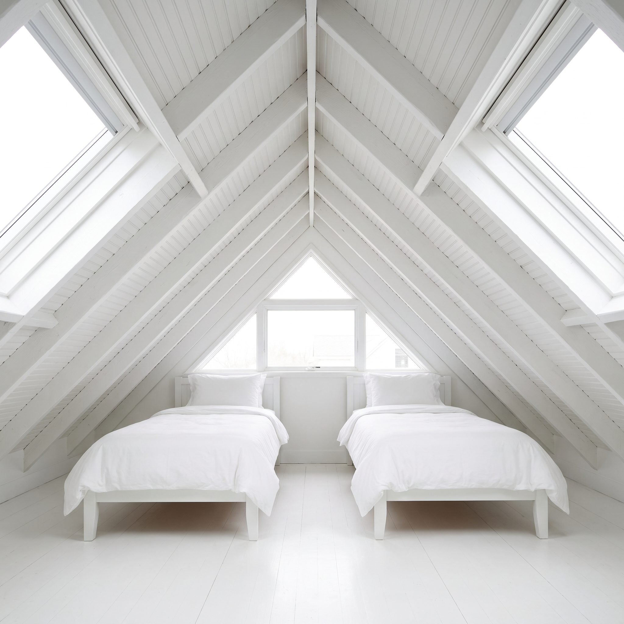 Twin guest bedroom with lavender upholstered beds beneath a steeply sloped gable ceiling