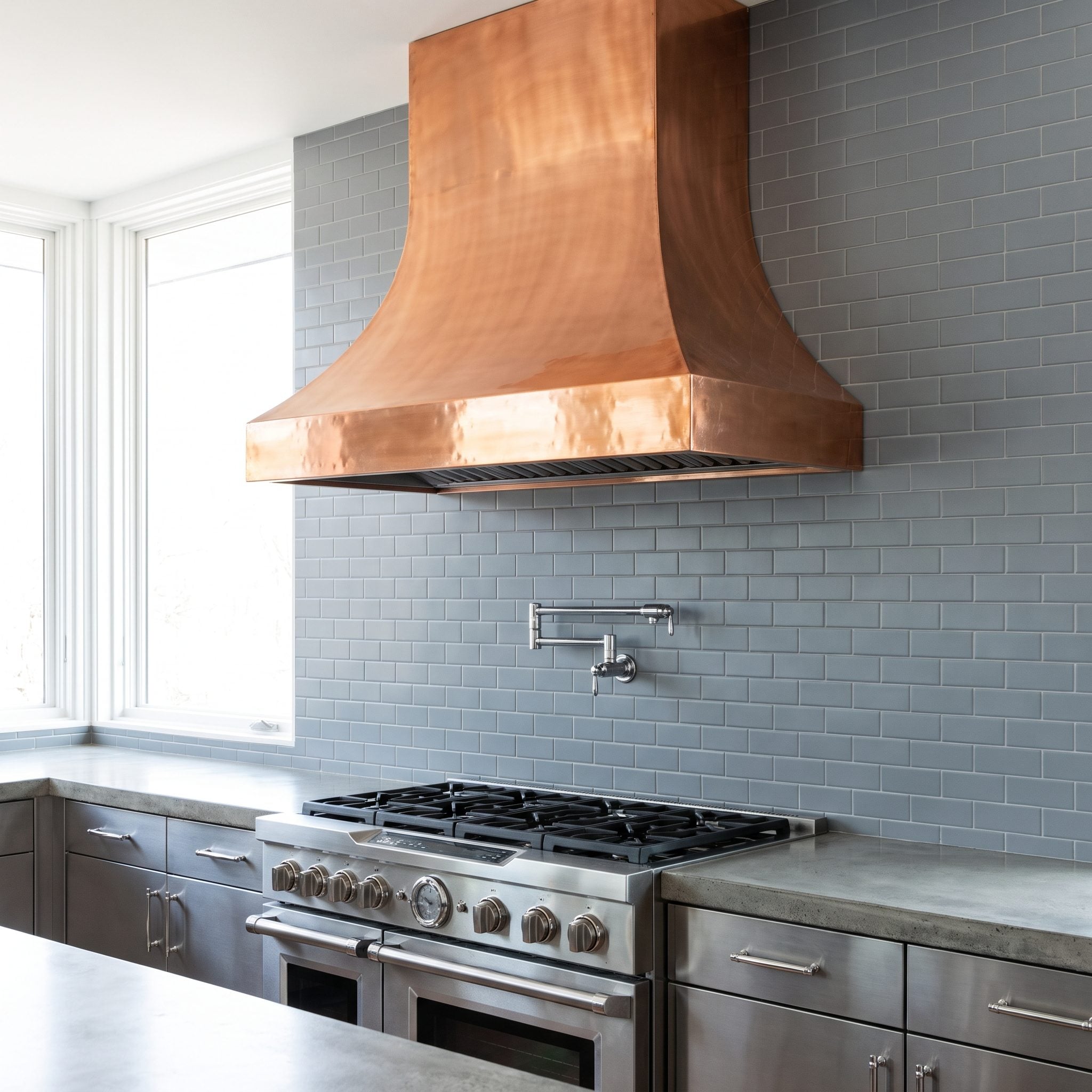 Kitchen renovation coordinating a copper range hood with warm-ivory backsplash tile and copper cabinet pulls