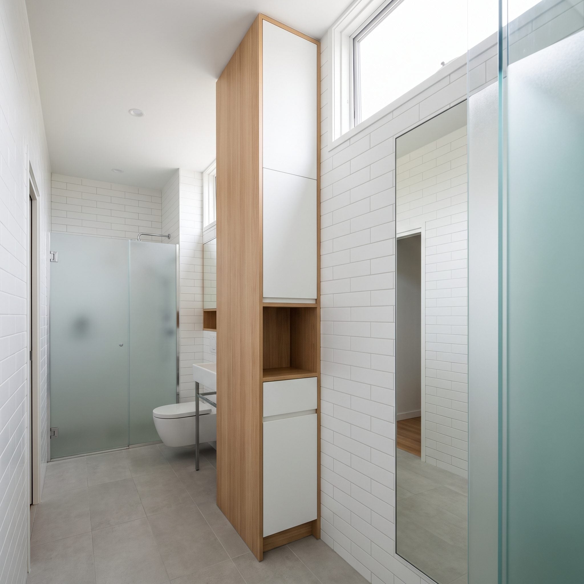 Bathroom with a tall storage cabinet and stacked open shelving using vertical wall space