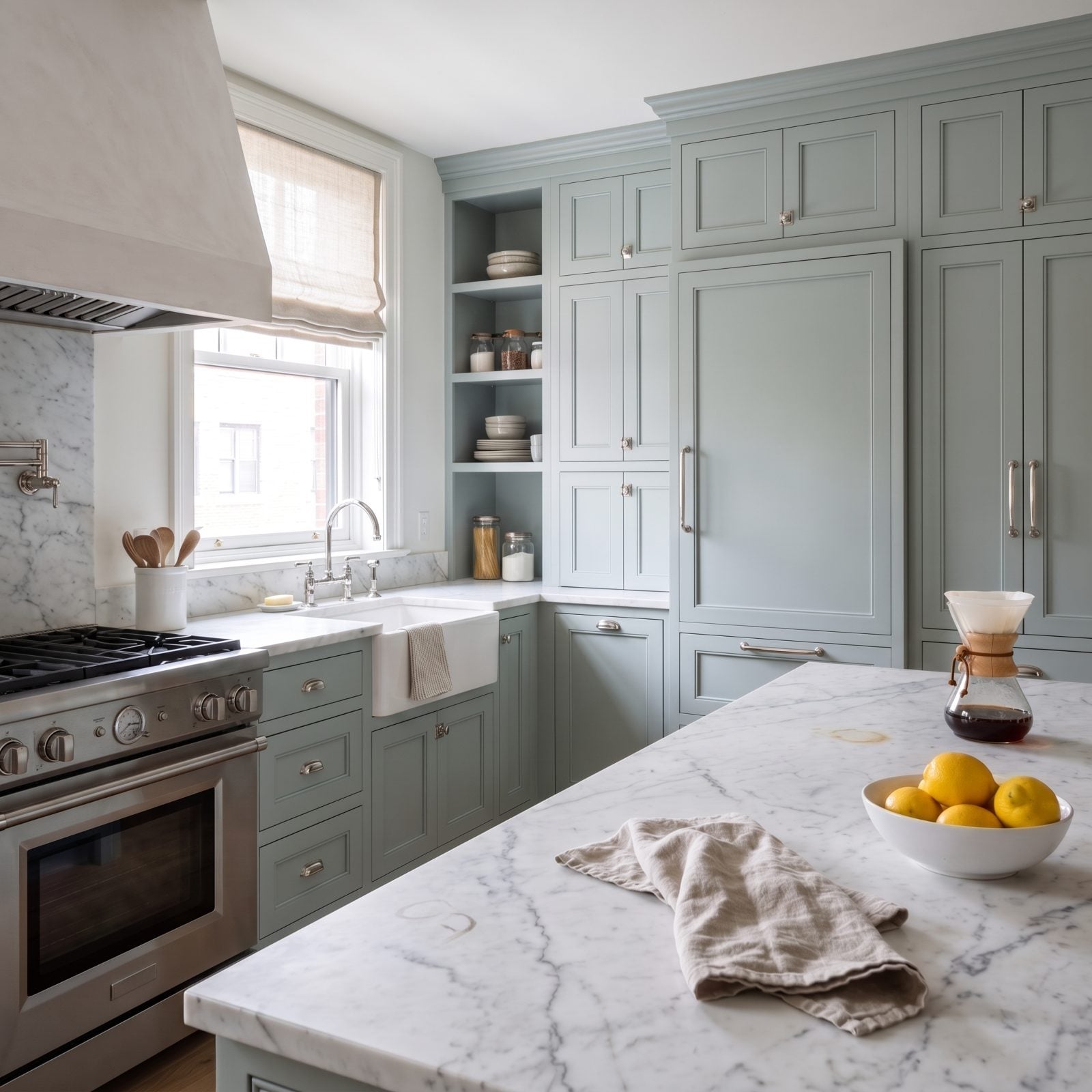 Blue-grey kitchen with white Carrara marble counters showing faint etch marks near the range and a small stain by the coffee
