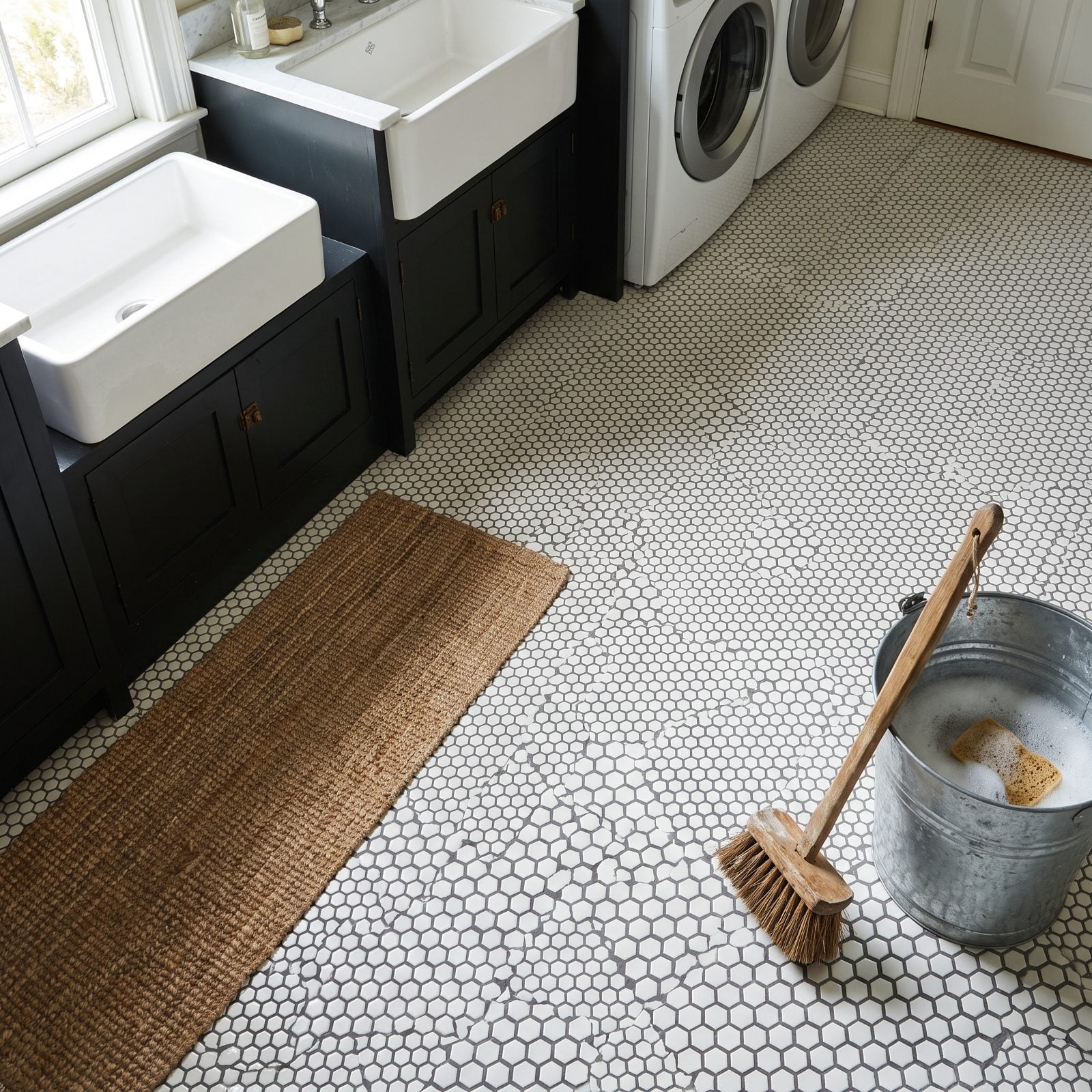 Bathroom floor in tiny white hexagon tile where the grout lines near the toilet and vanity have darkened to grey.