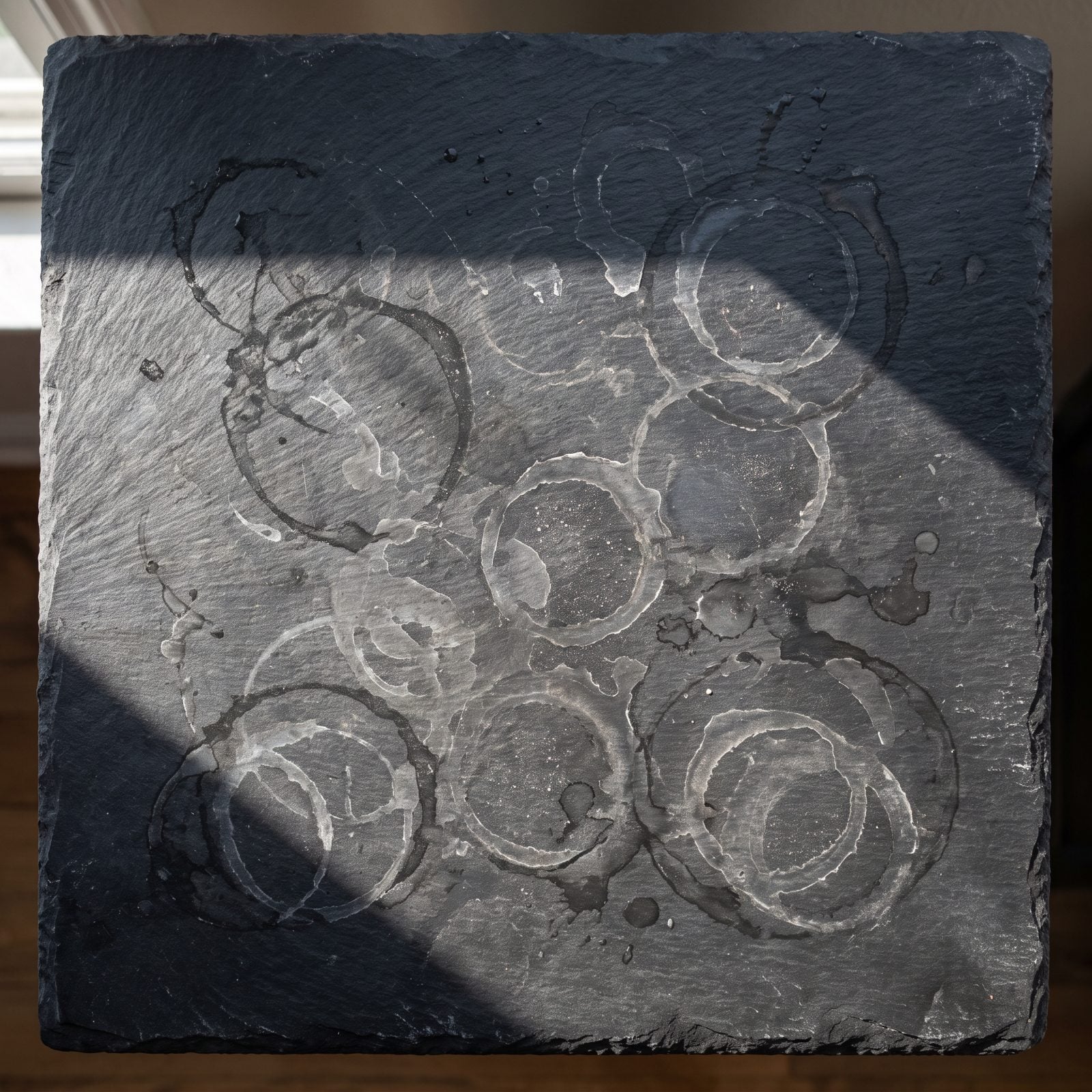 Dark bathroom countertop with a water glass sitting inside a faint ring of droplets to the left of the faucet, the right