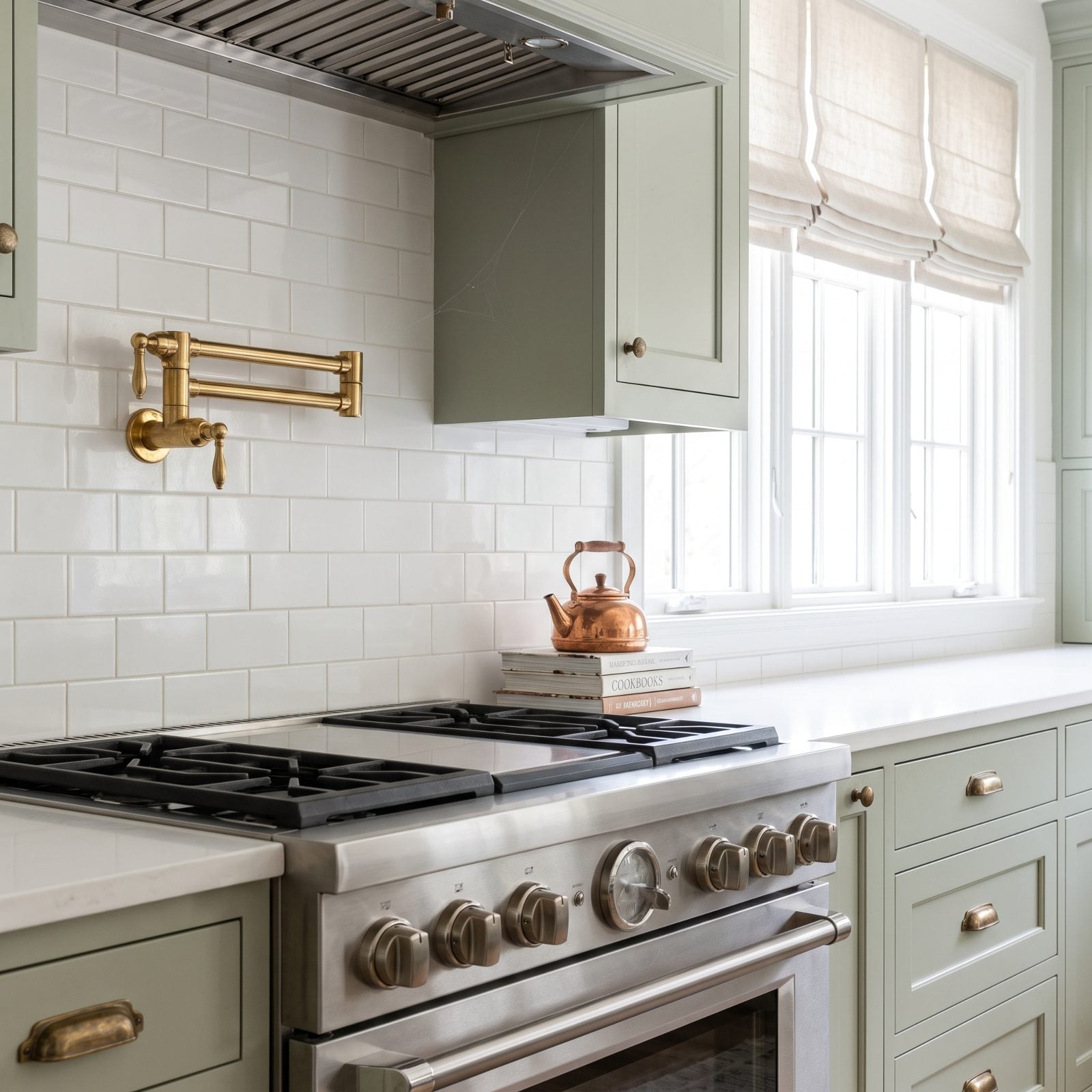 Dark green kitchen with a brass pot filler mounted above a professional range against subway tile.