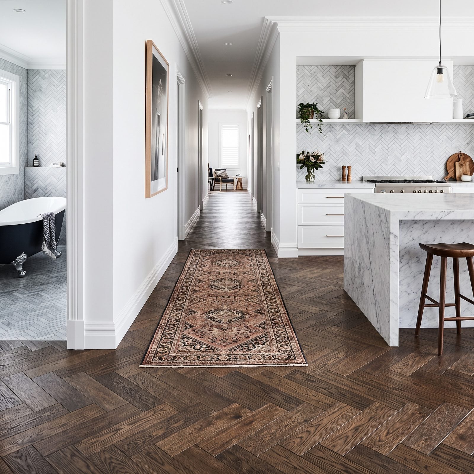 Oak herringbone flooring running through a narrow hallway and into a bedroom, creating a busy zigzag pattern.