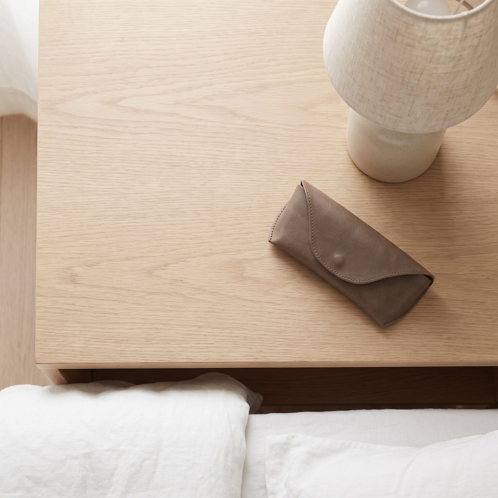 Bedroom nightstand holding one lamp and a single face-down paperback beside a queen bed.