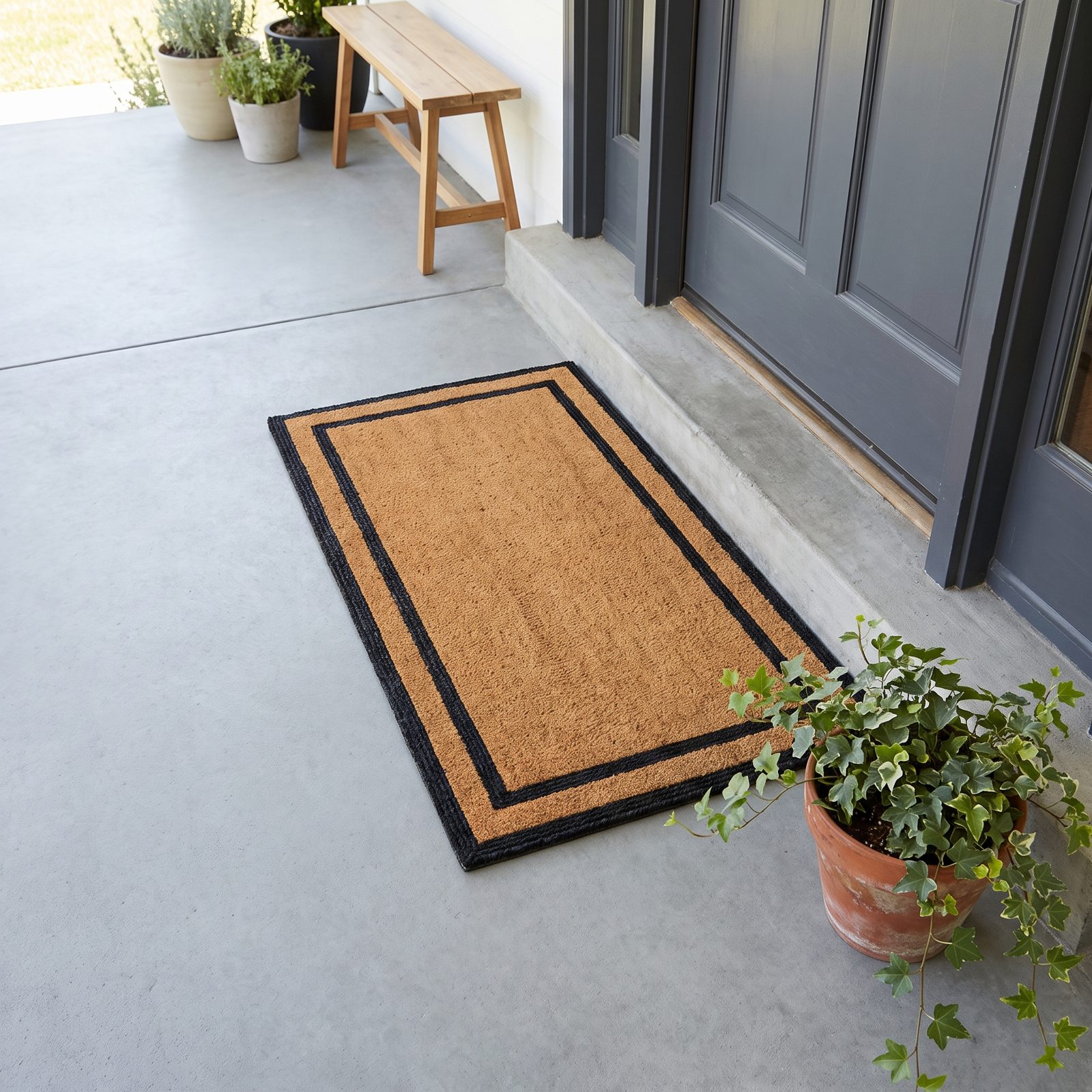 Doorstep with a new coir doormat squared to a charcoal-gray door and a potted ivy to the right.