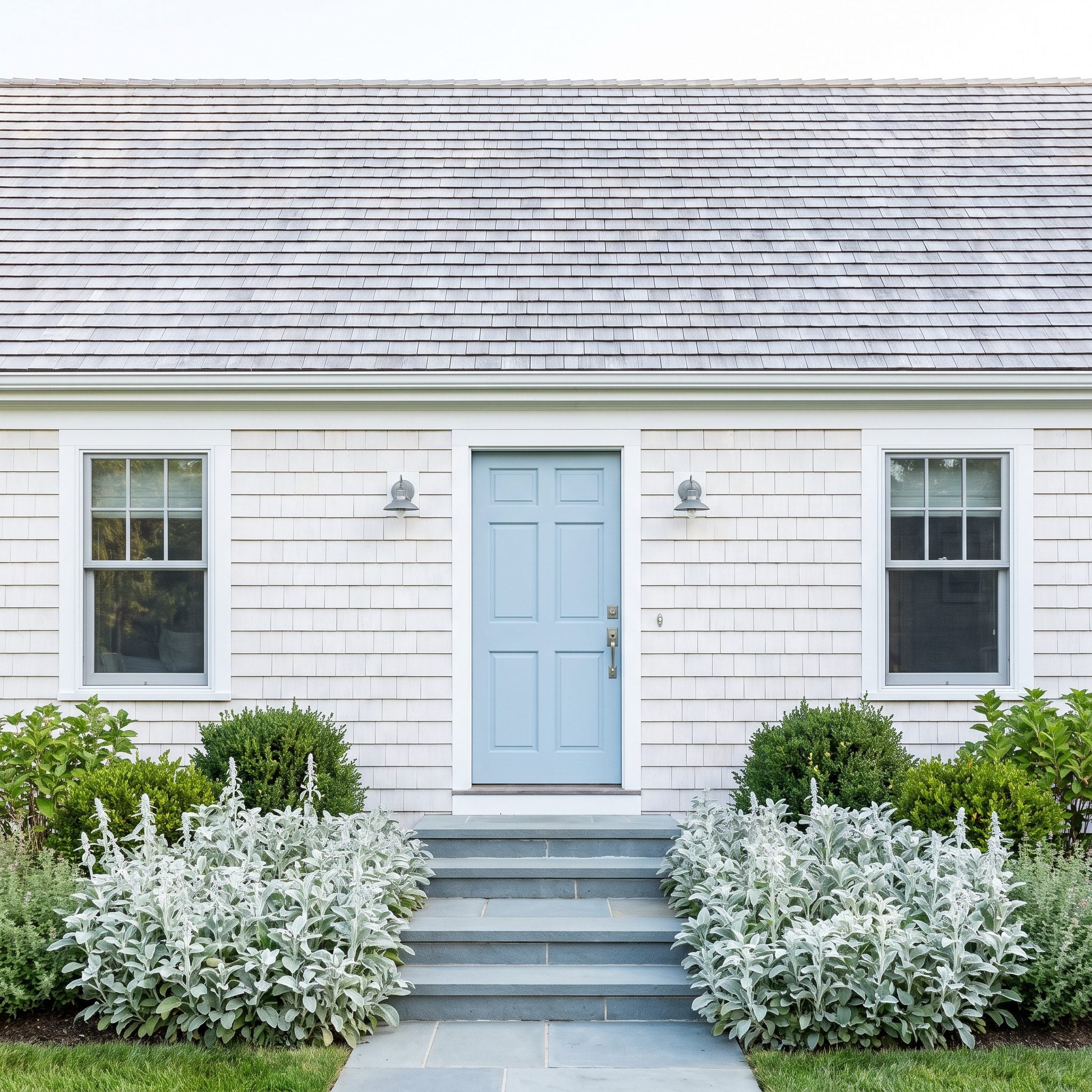 Powder-blue front door on a white Cape Cod home with gray roofing and pale stone steps