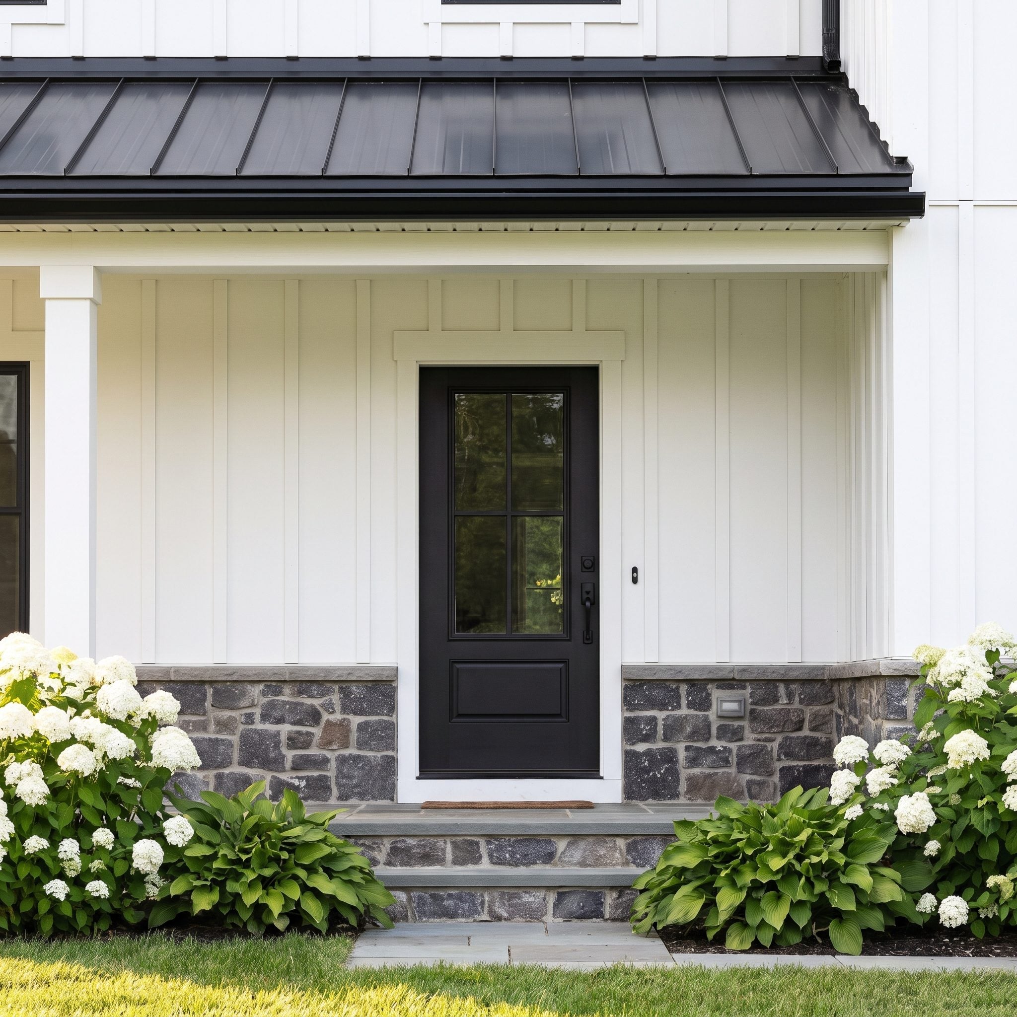 Soft-black farmhouse front door paired with white board-and-batten siding and a black metal roof
