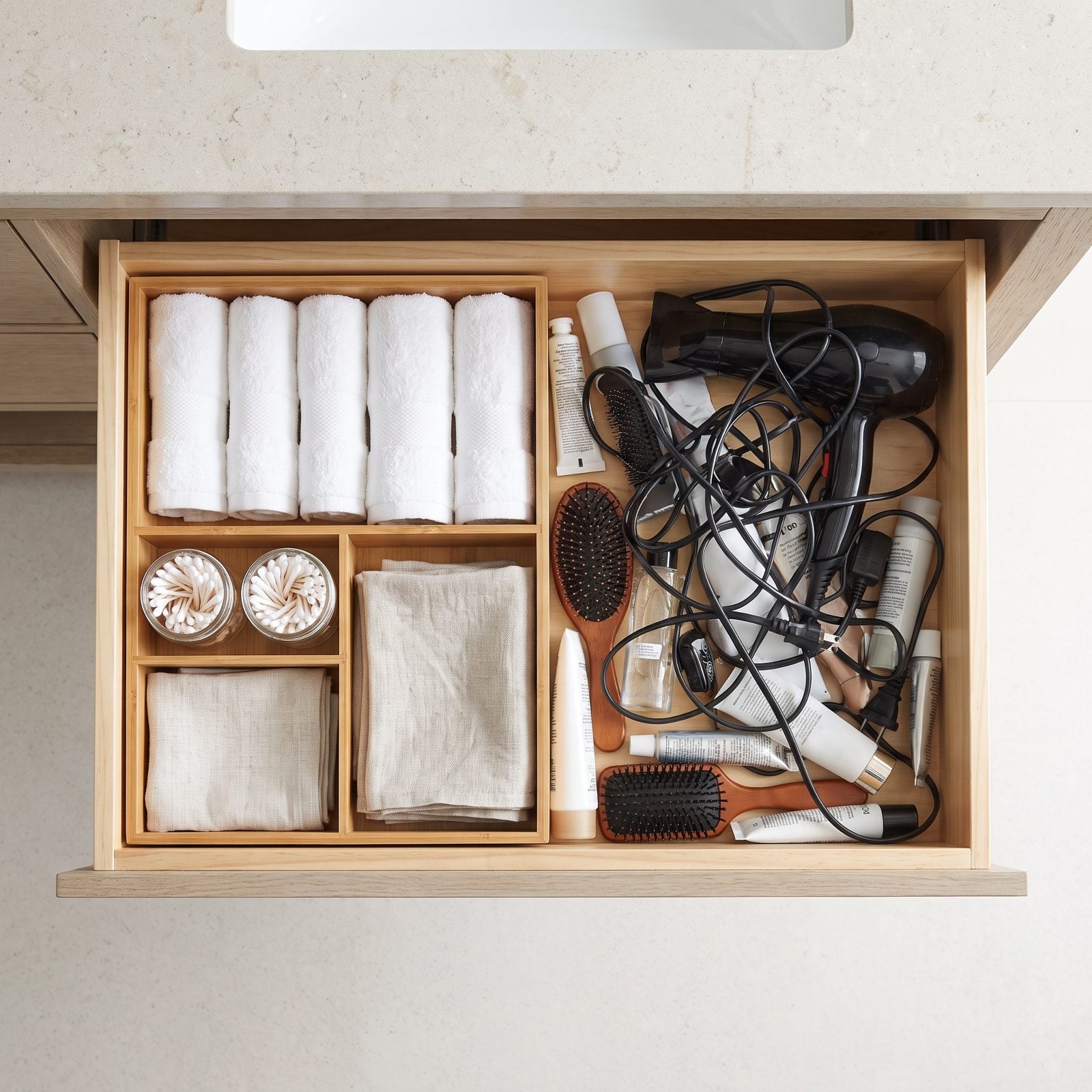 Open bathroom vanity drawer with a clear compartment organizer holding cotton swabs, sponges, lip balms, and small grooming