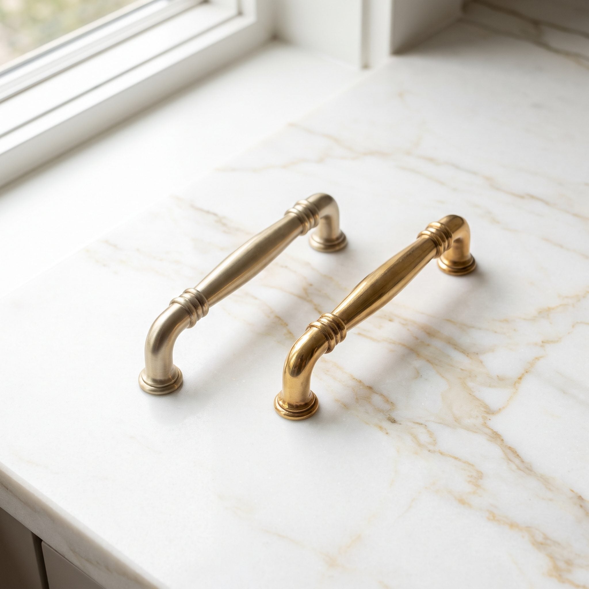 Cream kitchen with golden-veined quartzite and antique brass knobs, one resting on the stone for color matching.