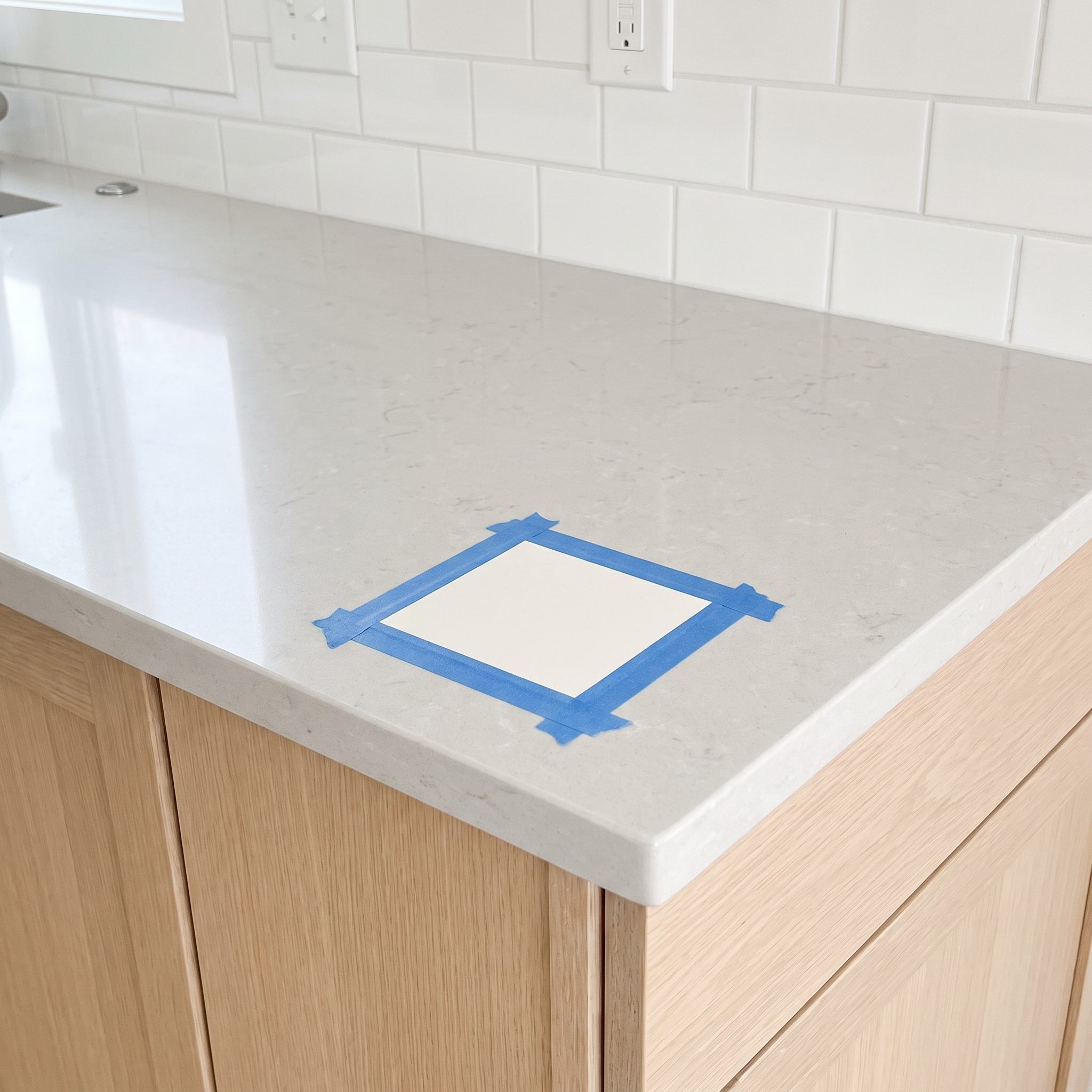 Kitchen with four large paint swatches taped to cabinet doors directly beneath a green granite countertop.