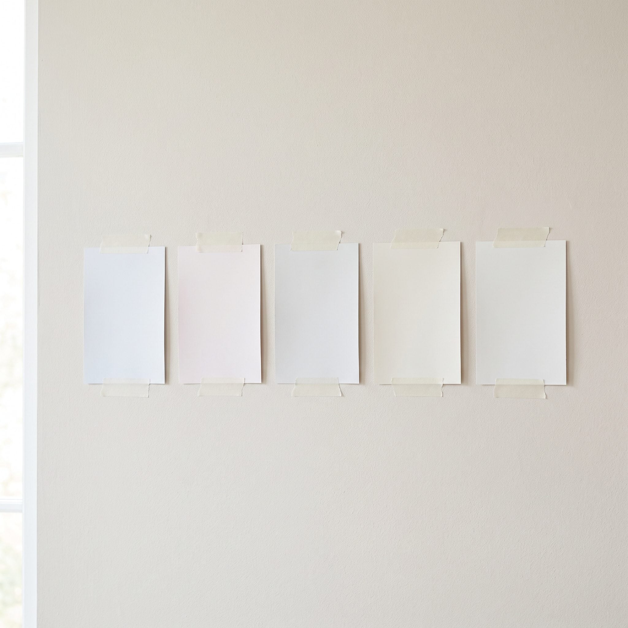 White kitchen with five slightly different white paint stripes tested side by side on a cabinet end panel.