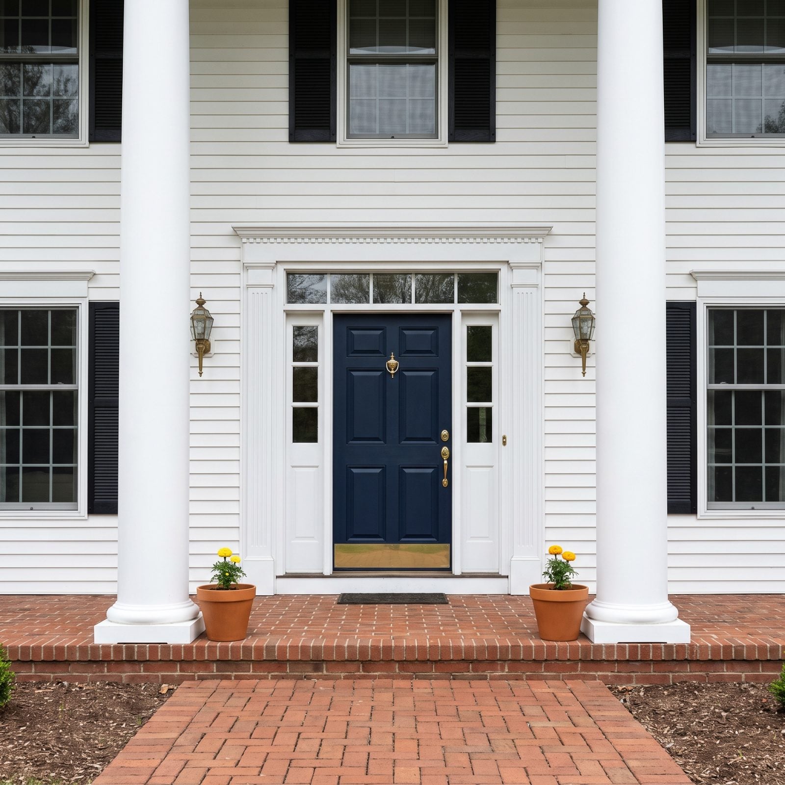 White colonial with a tall navy front door flanked by two small ten-inch terracotta pots.