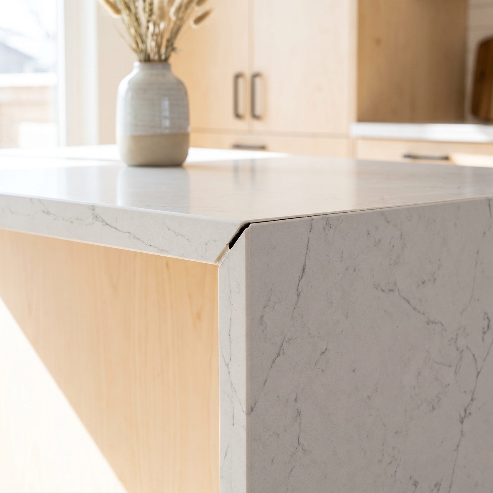 Close-up of a waterfall island quartz miter joint that has opened to a thin dark gap at the outer corner.