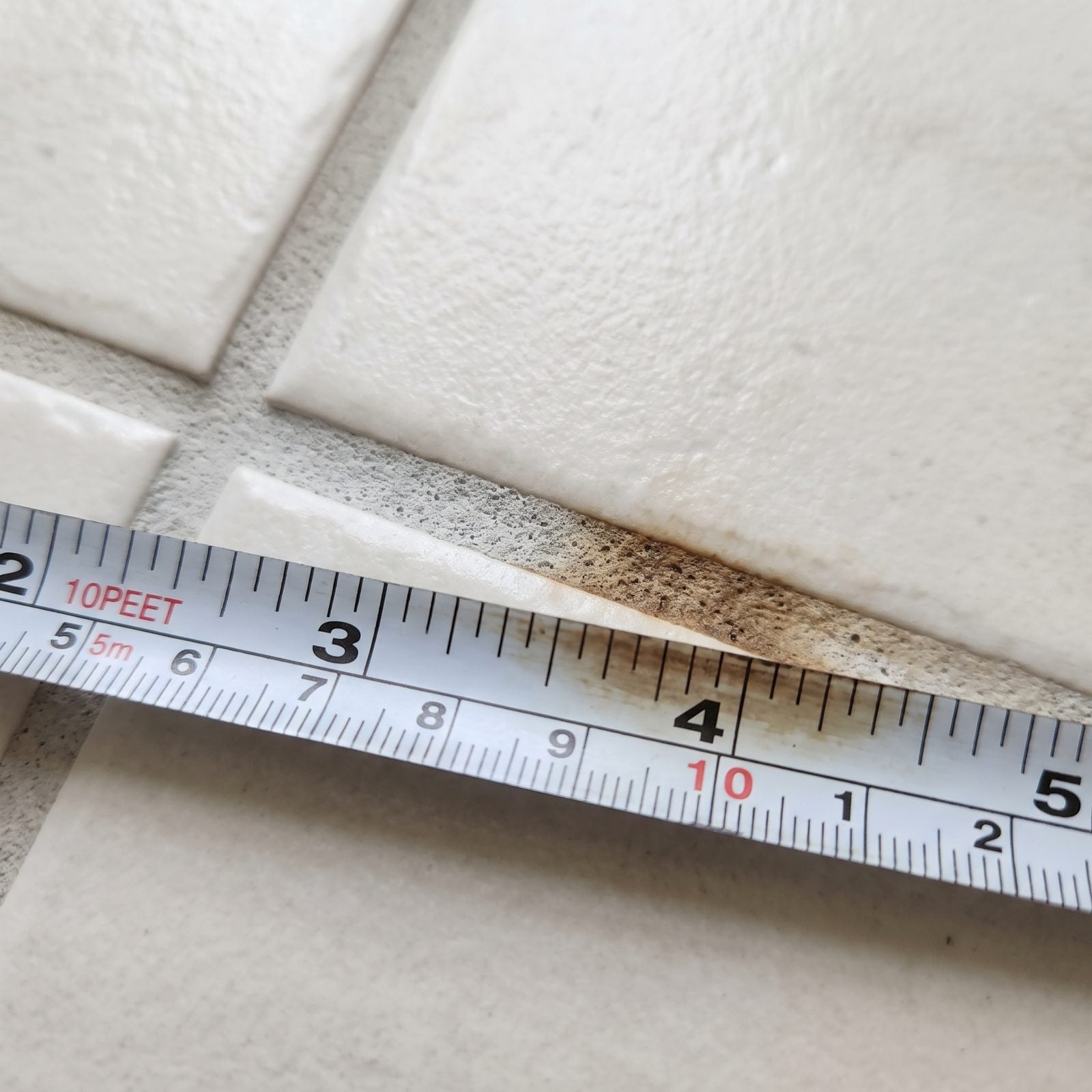 Close view of white subway tile above a bathroom vanity with clean pale-gray grout lines and a caulk seam at the counter.