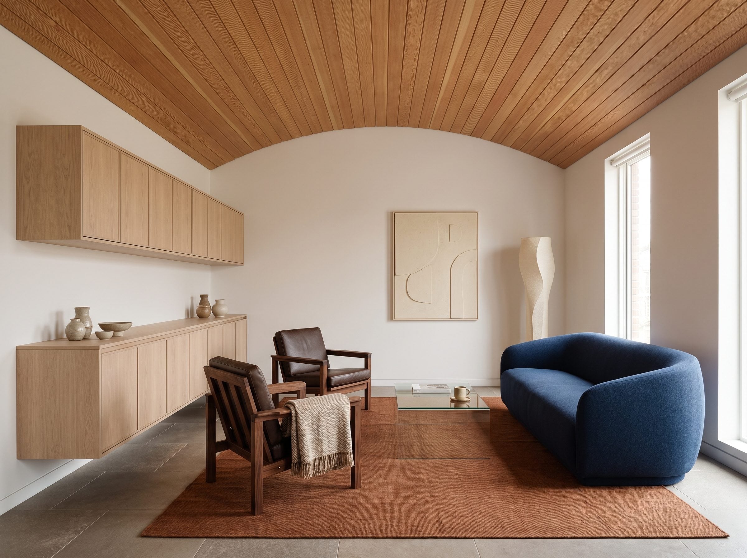 Living room with barrel-vaulted cedar ceiling, pale oak cabinetry, walnut chairs, and navy bouclé sofa