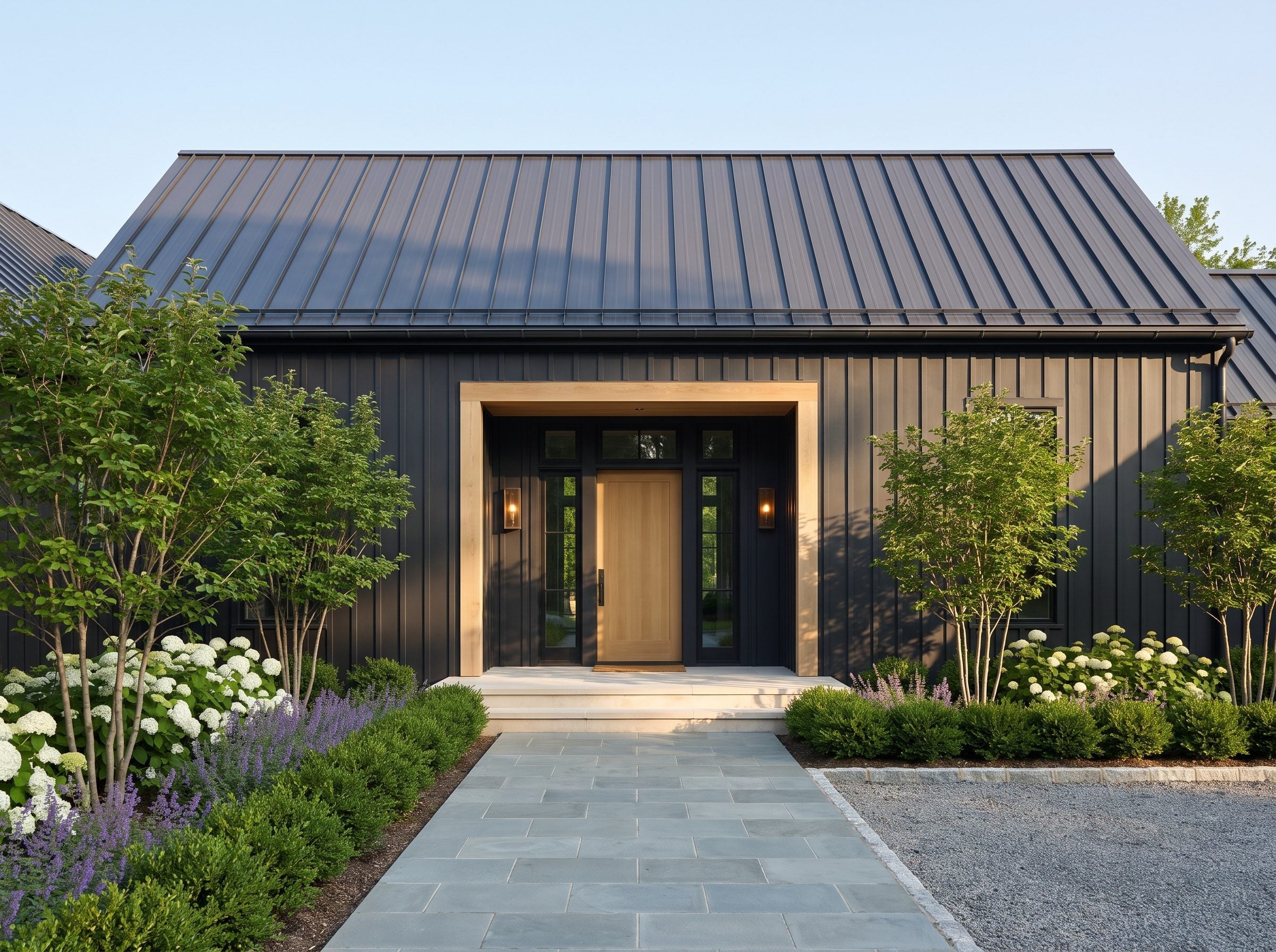 Dark standing-seam metal house with a natural wood entry surround and landscaped stone walkway
