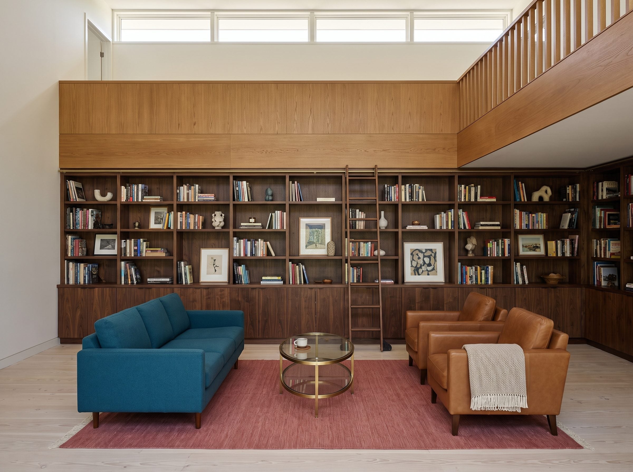 Double-height library with dark walnut lower bookcases, lighter upper cabinetry, brass rolling ladder, and pale flooring