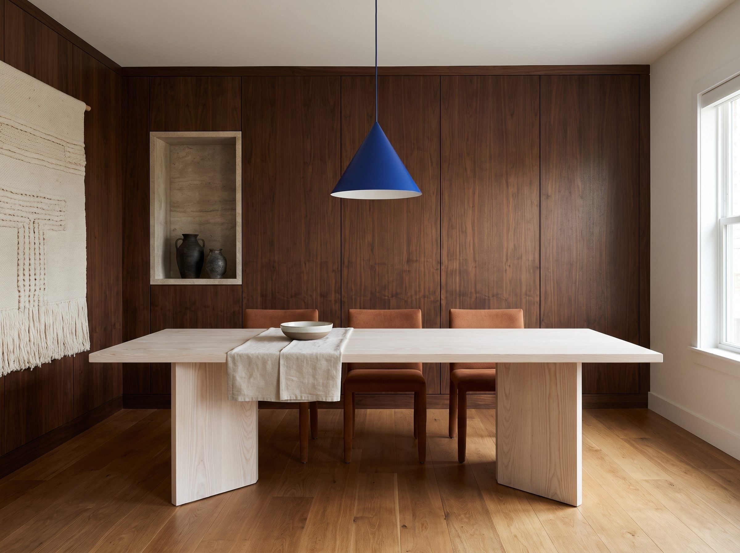 Dining room with cobalt pendant, dark walnut wall paneling, pale ash dining table, and cognac leather chairs