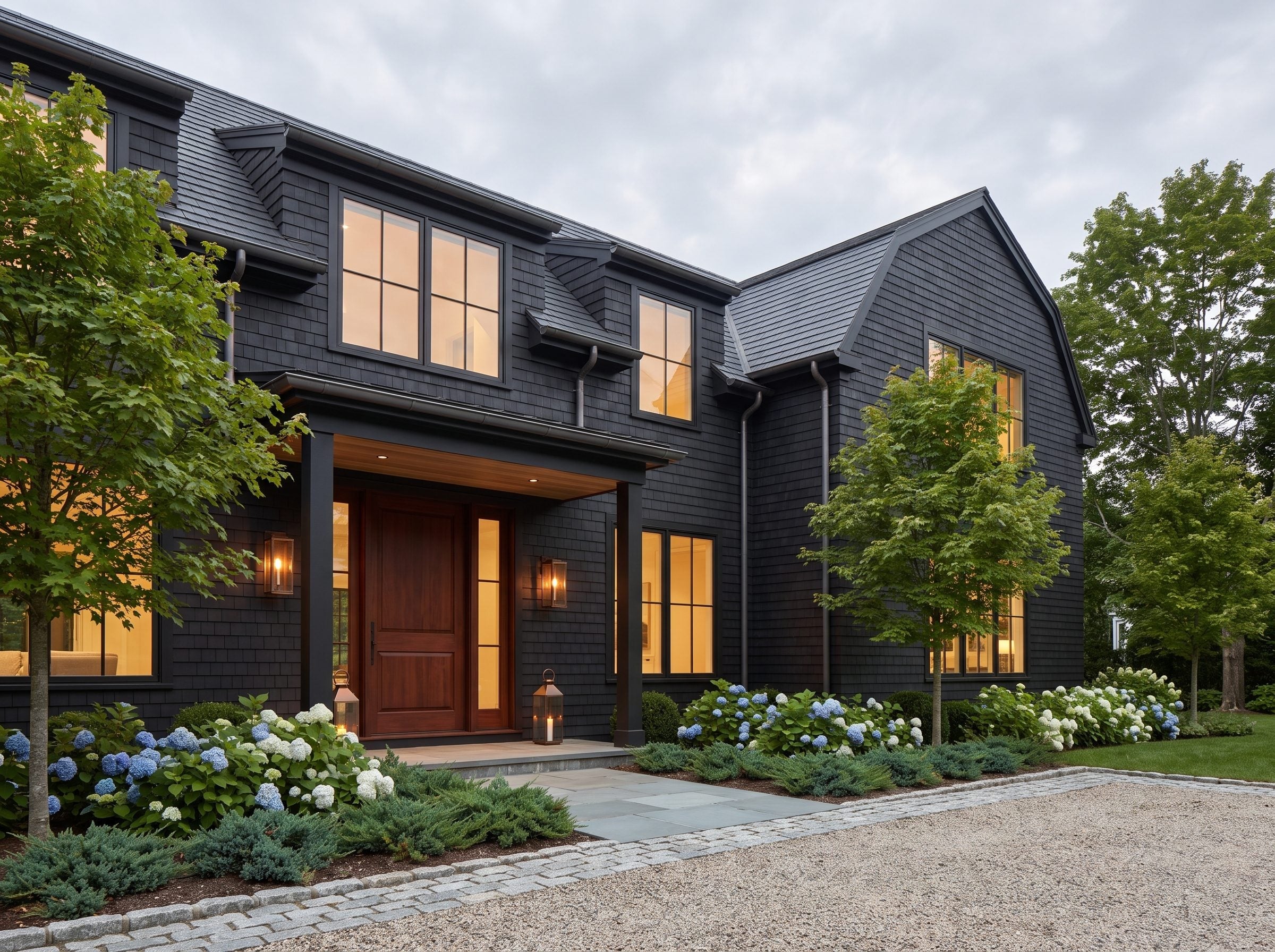 Charcoal shingle house with a wood entrance and beds of blue and white hydrangeas