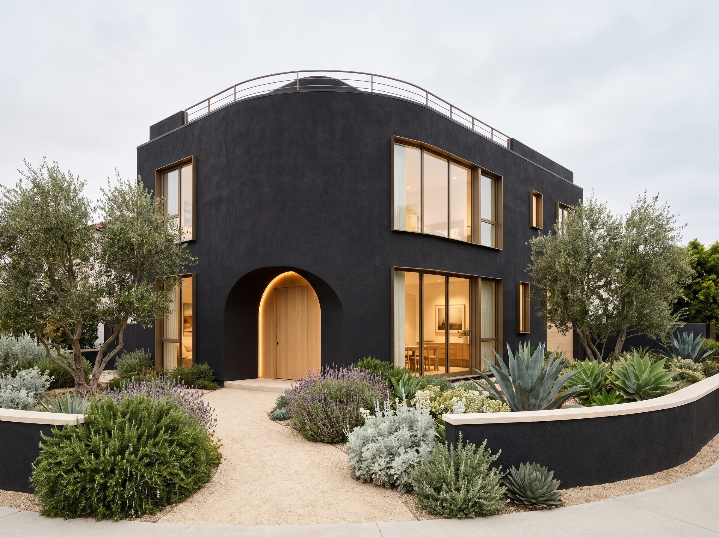 Black stucco house with rounded corners, an arched entry, and Mediterranean-style planting