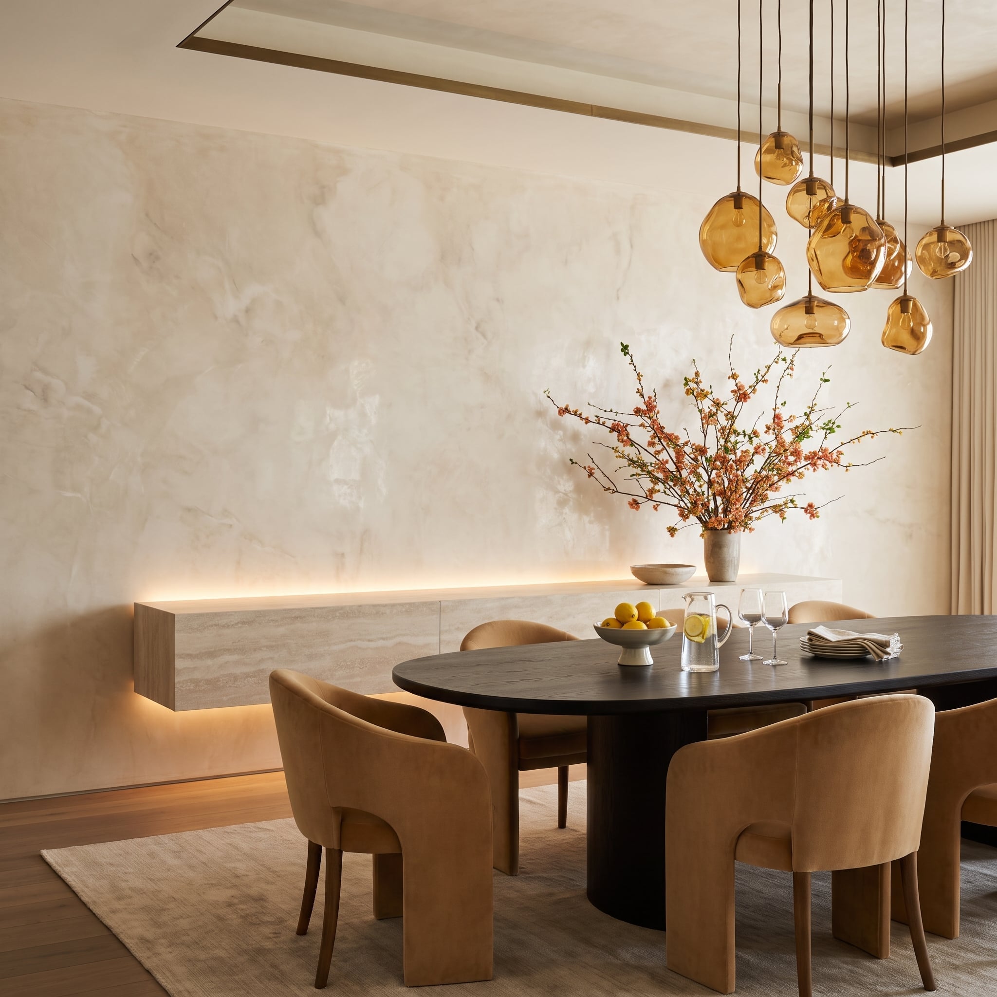 Warm limewash dining room accent wall with amber glass pendants and caramel velvet chairs