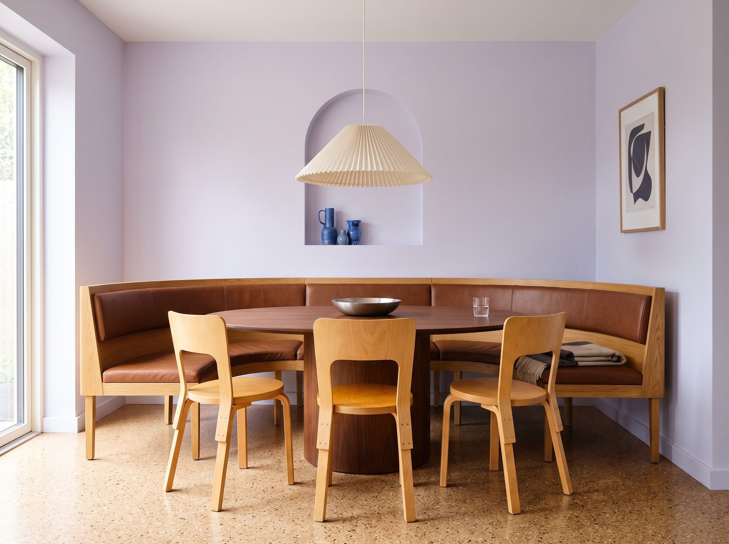 Dining nook with curved oak banquette, walnut pedestal table, light birch chairs, and soft accent colors