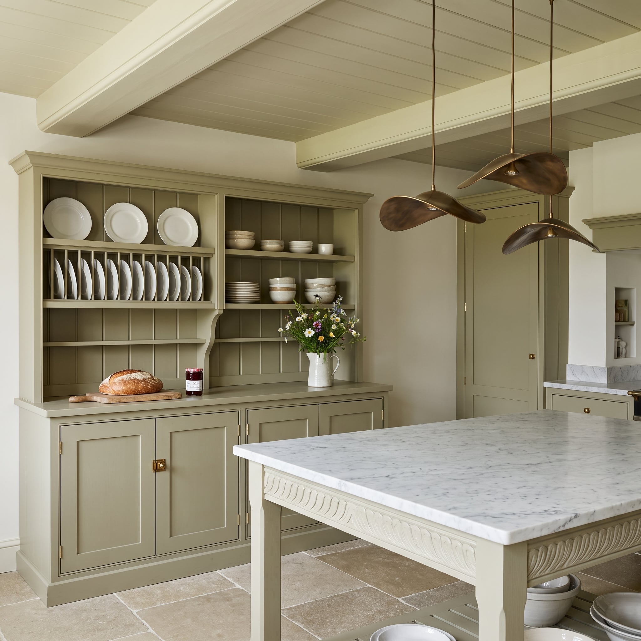 Sage-green kitchen with built-in upright plate rack, beadboard backing, marble island, and brass pendants