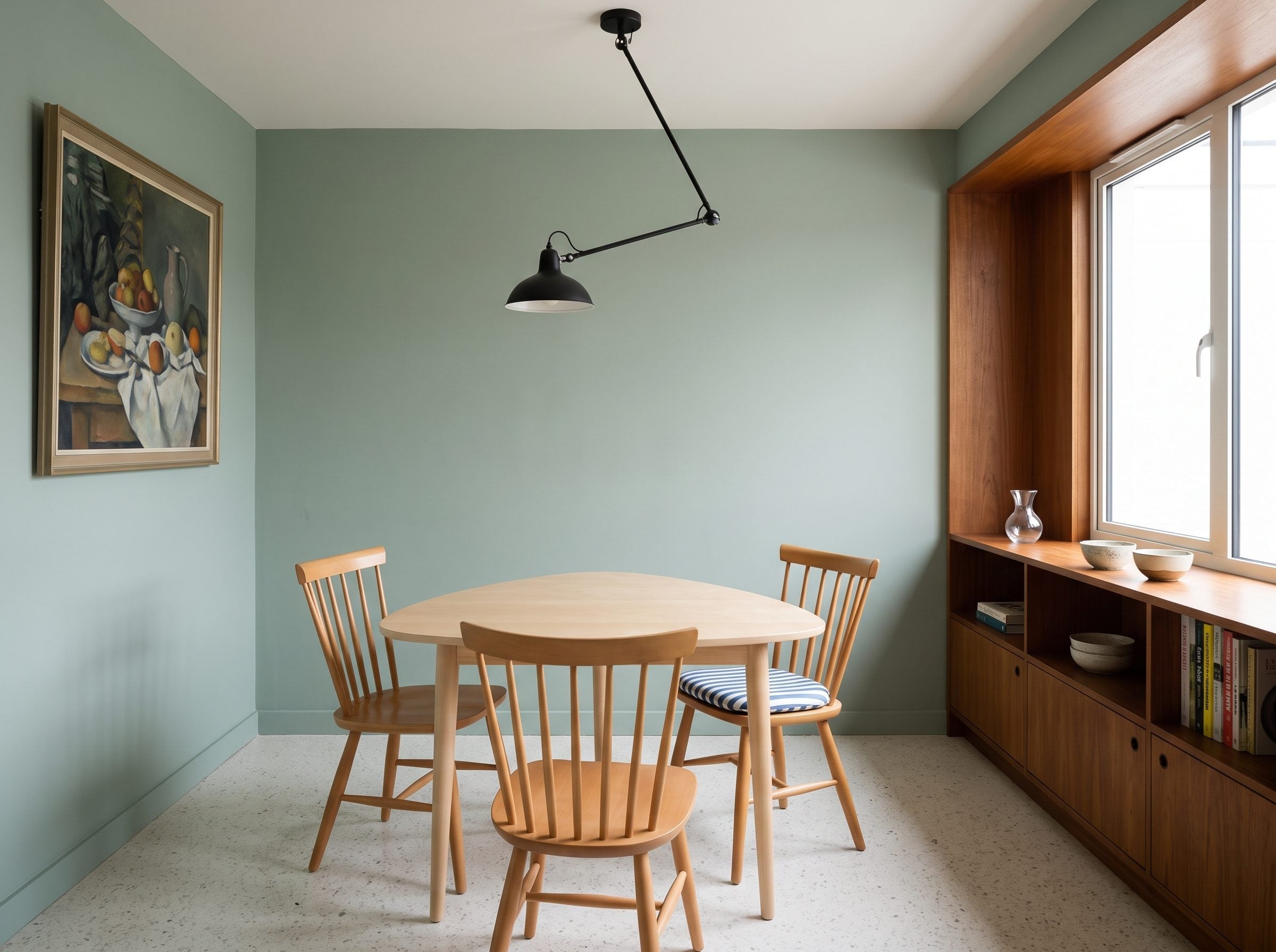 Compact dining room with sage walls, pale beech furniture, dark wood shelving, and black articulated ceiling light