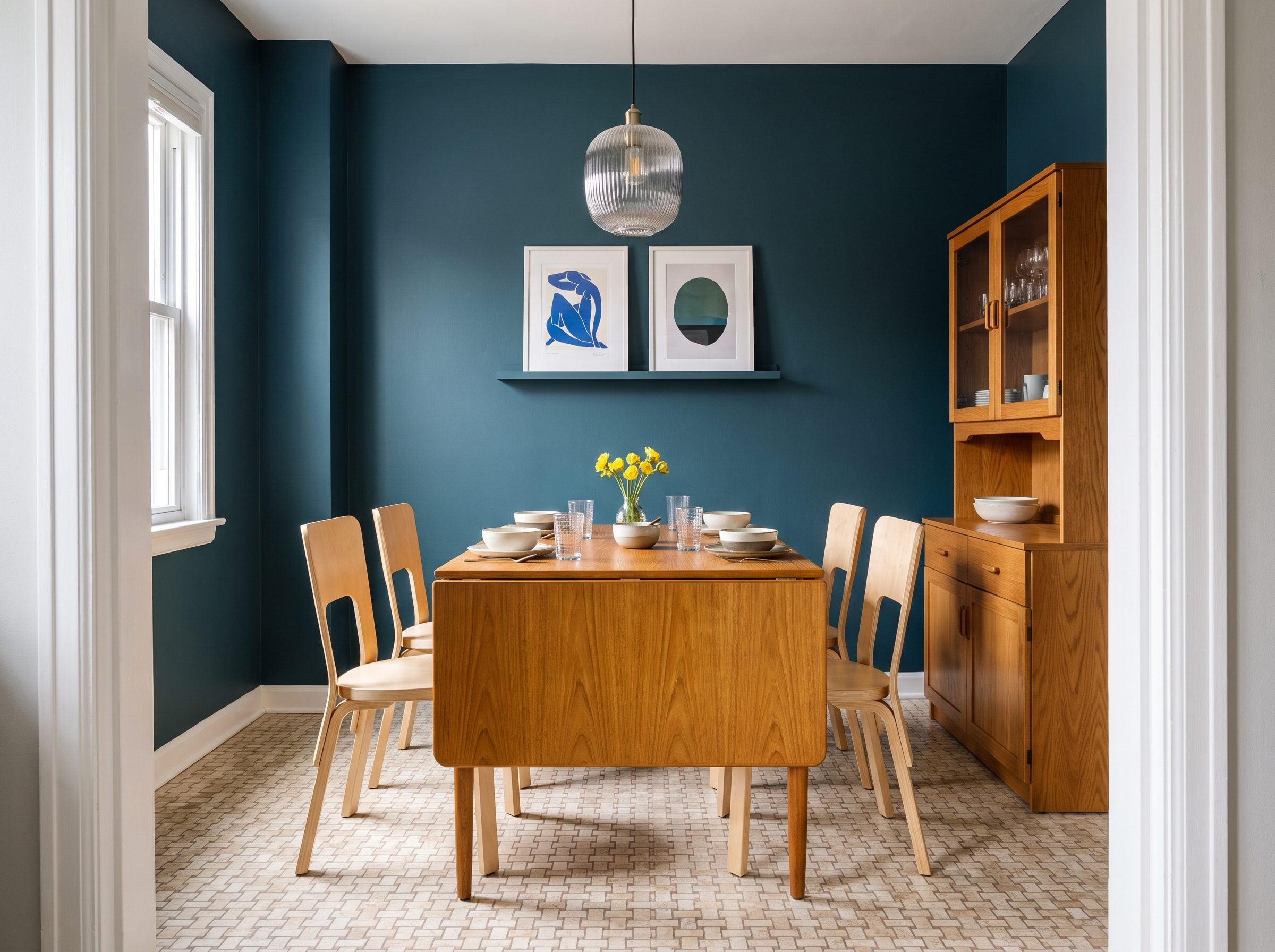 Dining room with deep teal walls, walnut drop-leaf table, dark wood hutch, and pale birch chairs