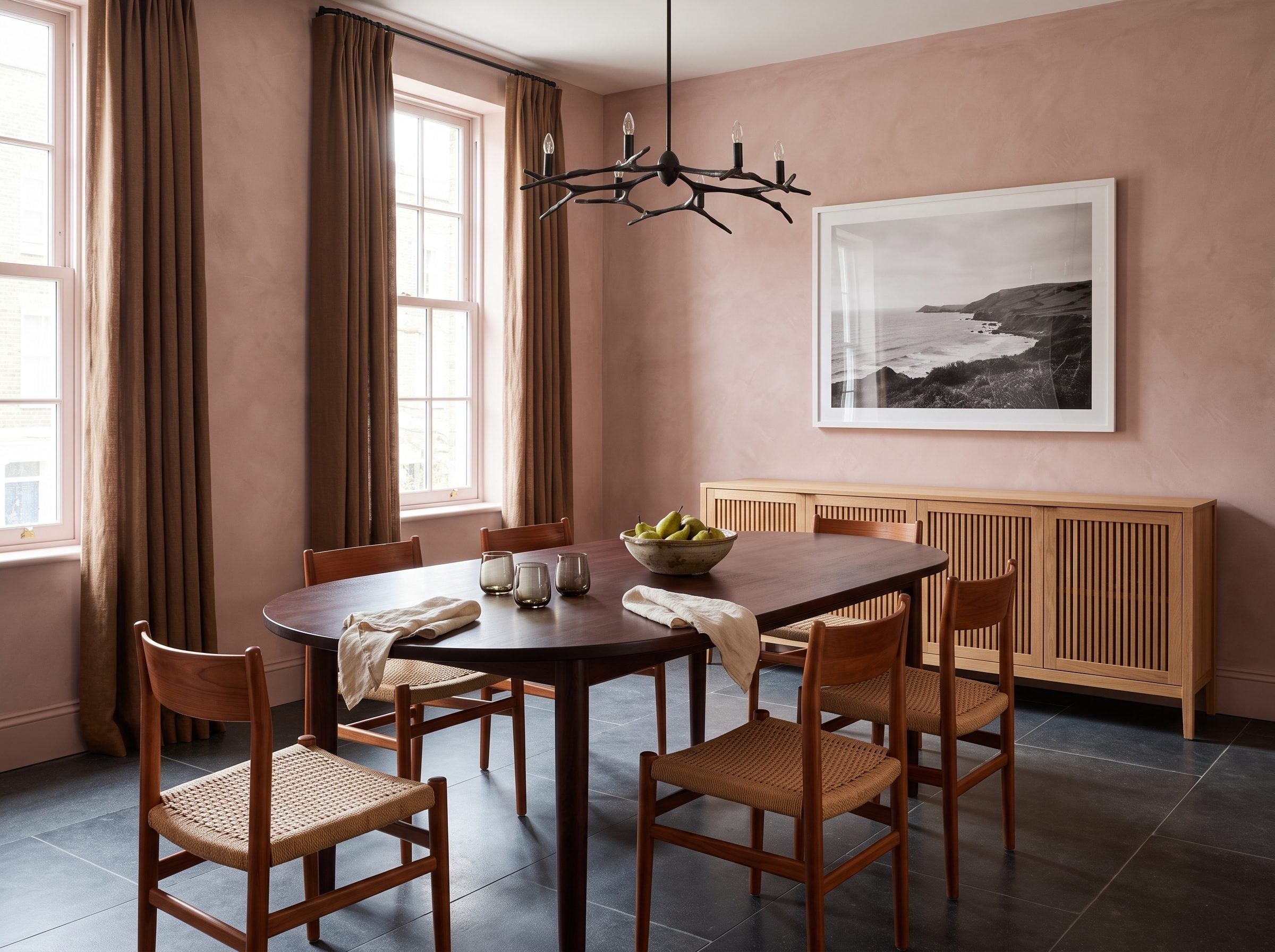 Dining room with dusty pink plaster walls, walnut table, oak sideboard, and rattan chairs